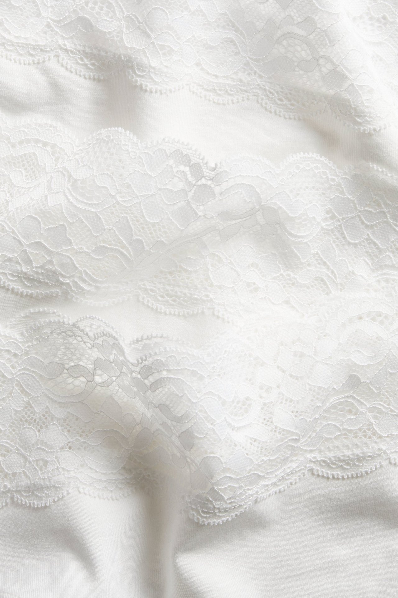 Nærbilde av hvit bomullsstringtruse med intrikate hvite blondedetaljer.