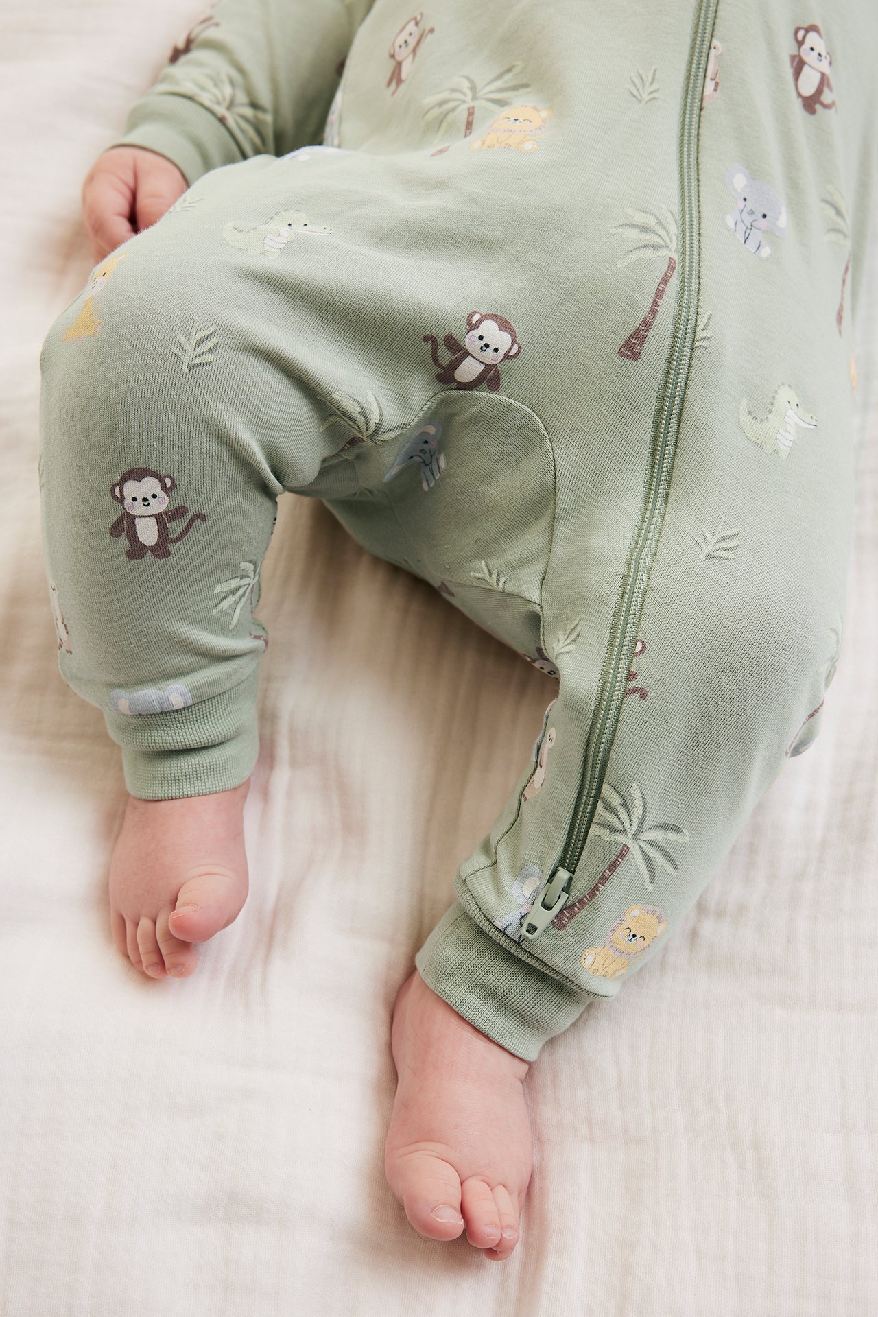 Zbliżenie na dziecko w zielonym romperze w zwierzęcy wzór, zapinanym na praktyczny dwukierunkowy suwak.