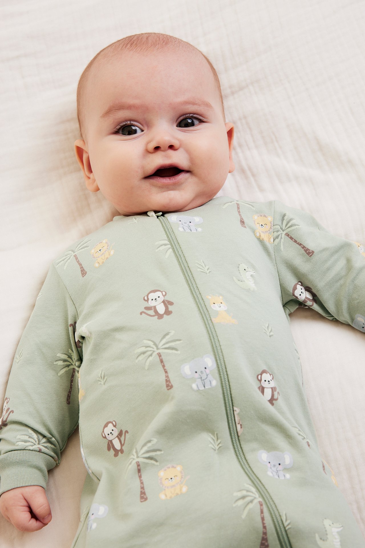 Widok z przodu: Niemowlę w zielonym pajacyku w zwierzęcy wzór z dwukierunkowym zamkiem.