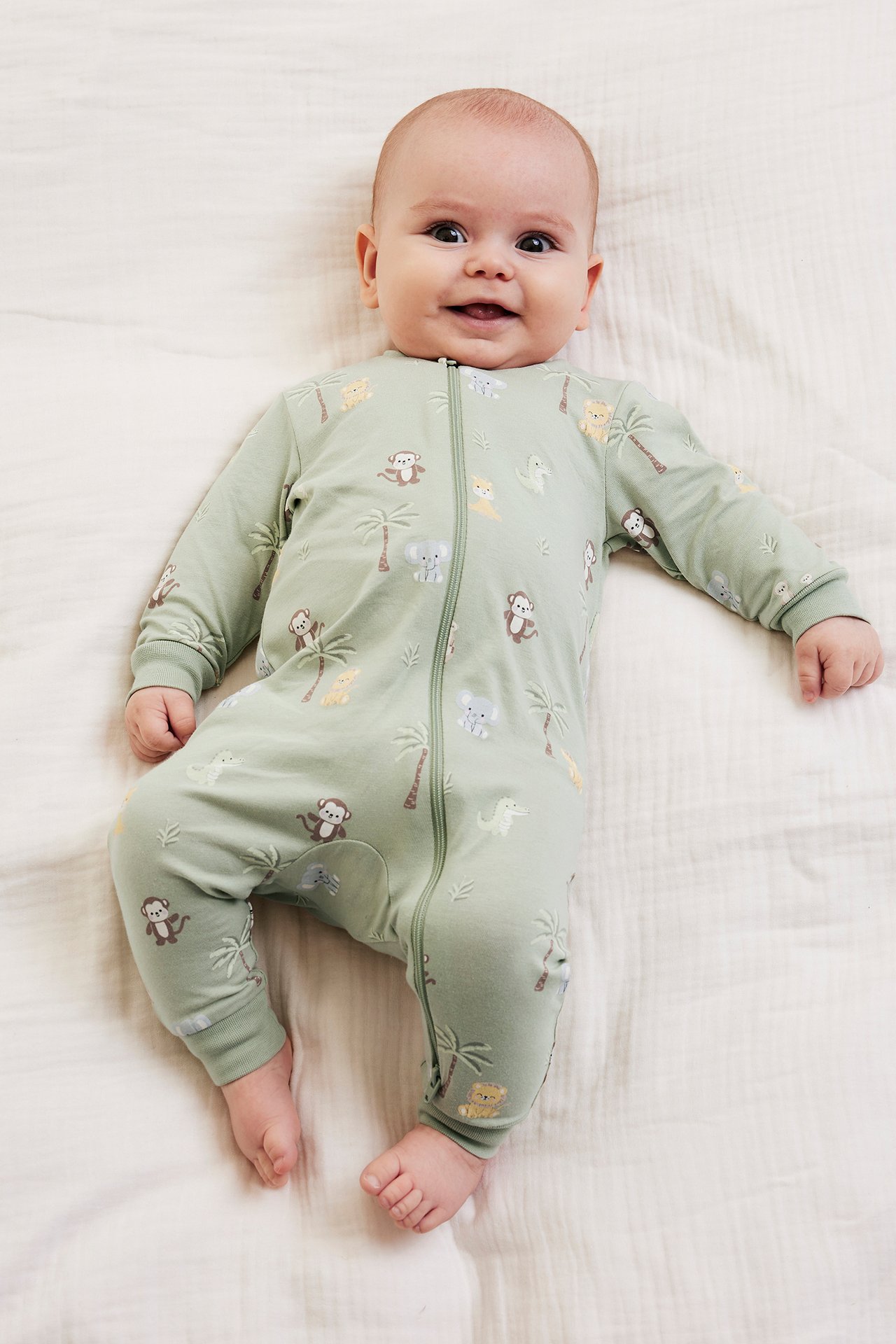 Framsida på en leende bebis i en ljusgrön djurmönstrad pyjamas med tvåvägsdragkedja framtill.