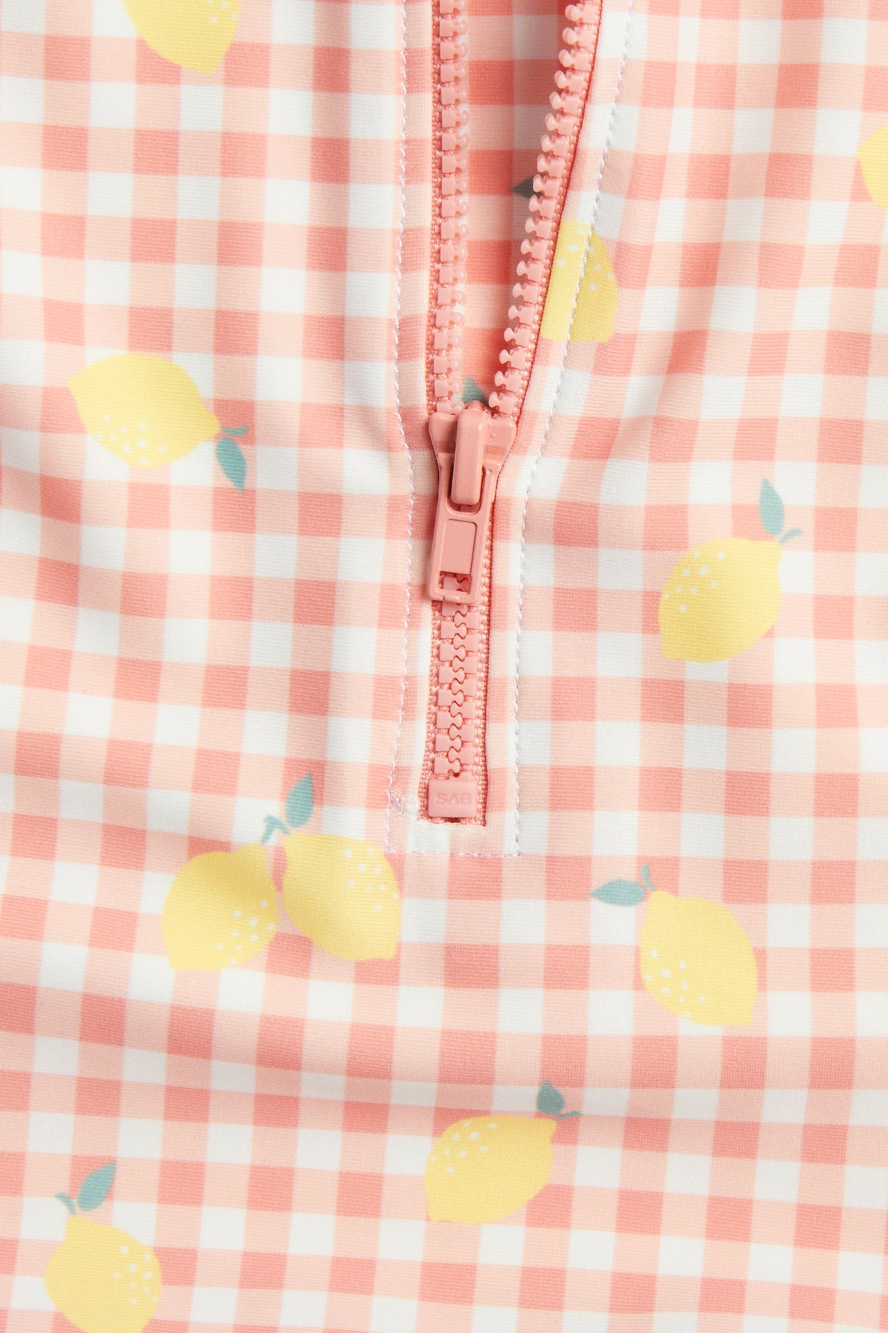 Närbild på babys rosa rutiga långärmade baddräkt med gula citroner och rosa dragkedja.