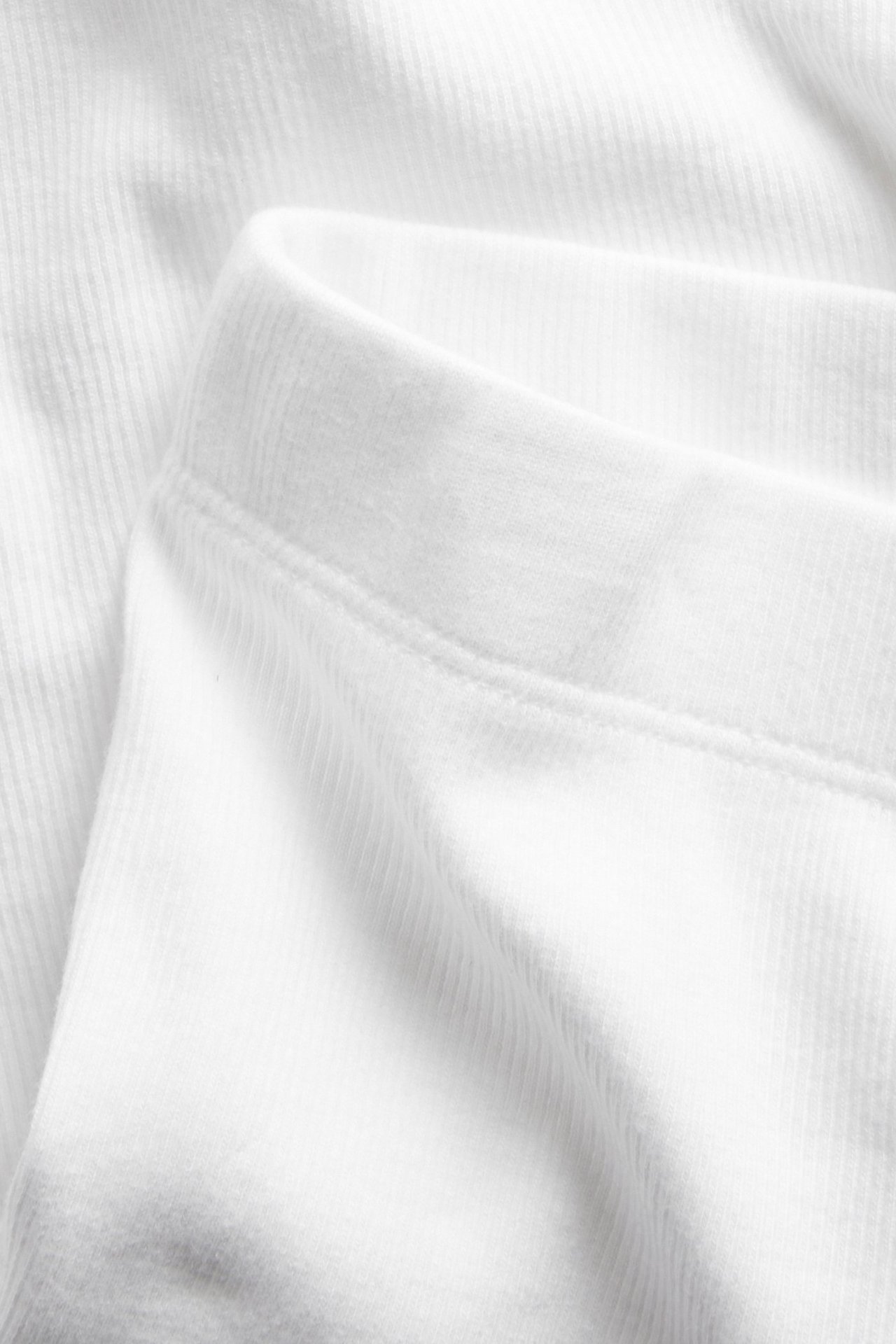 Zbliżenie białych prążkowanych szortów rowerowych, ukazujące miękki materiał z bawełny z elastanem i elastyczny pas.