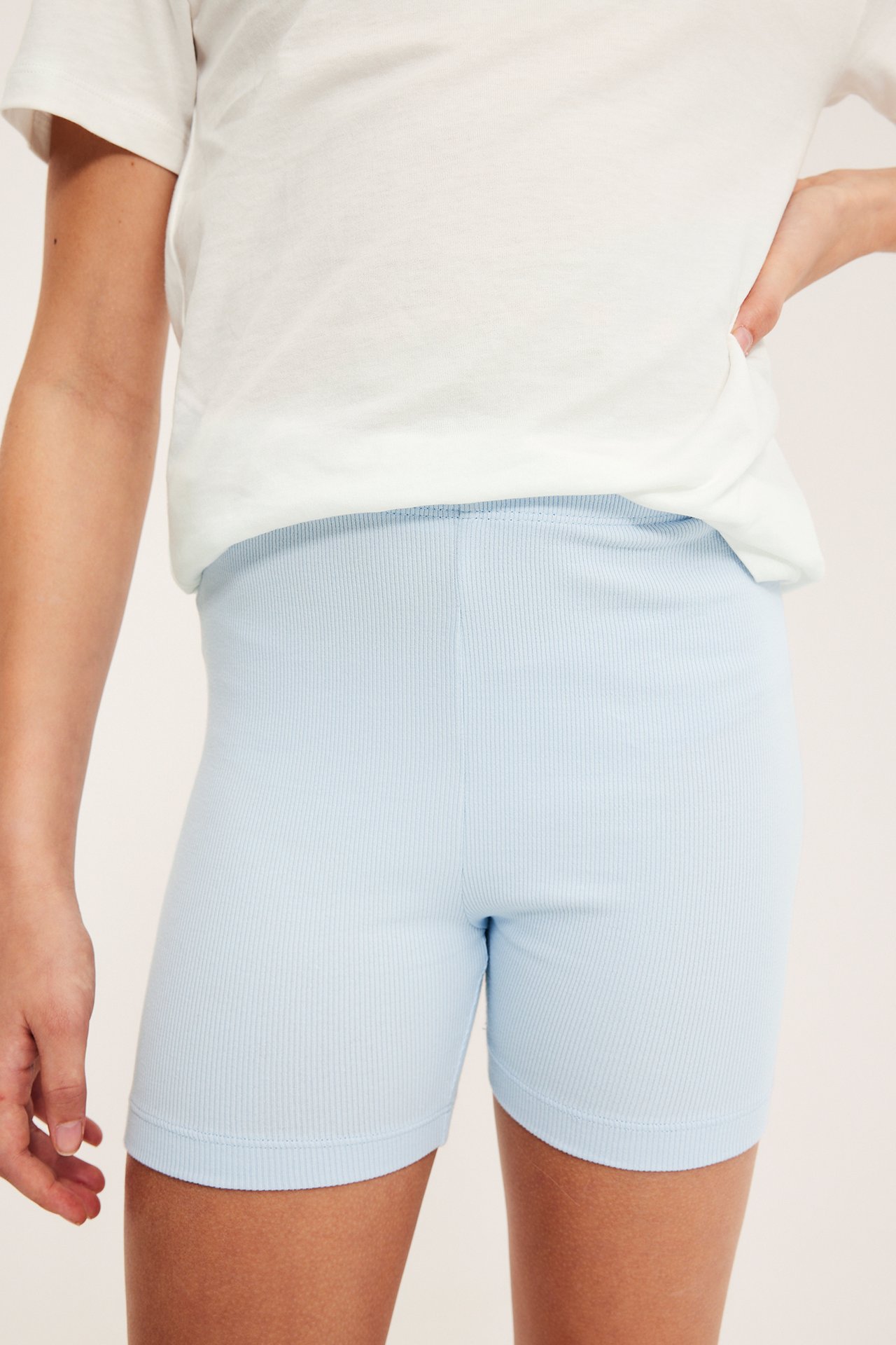 Forfra, et barn i lyseblå ribbestrikkede sykkelshorts og en hvit t-skjorte.