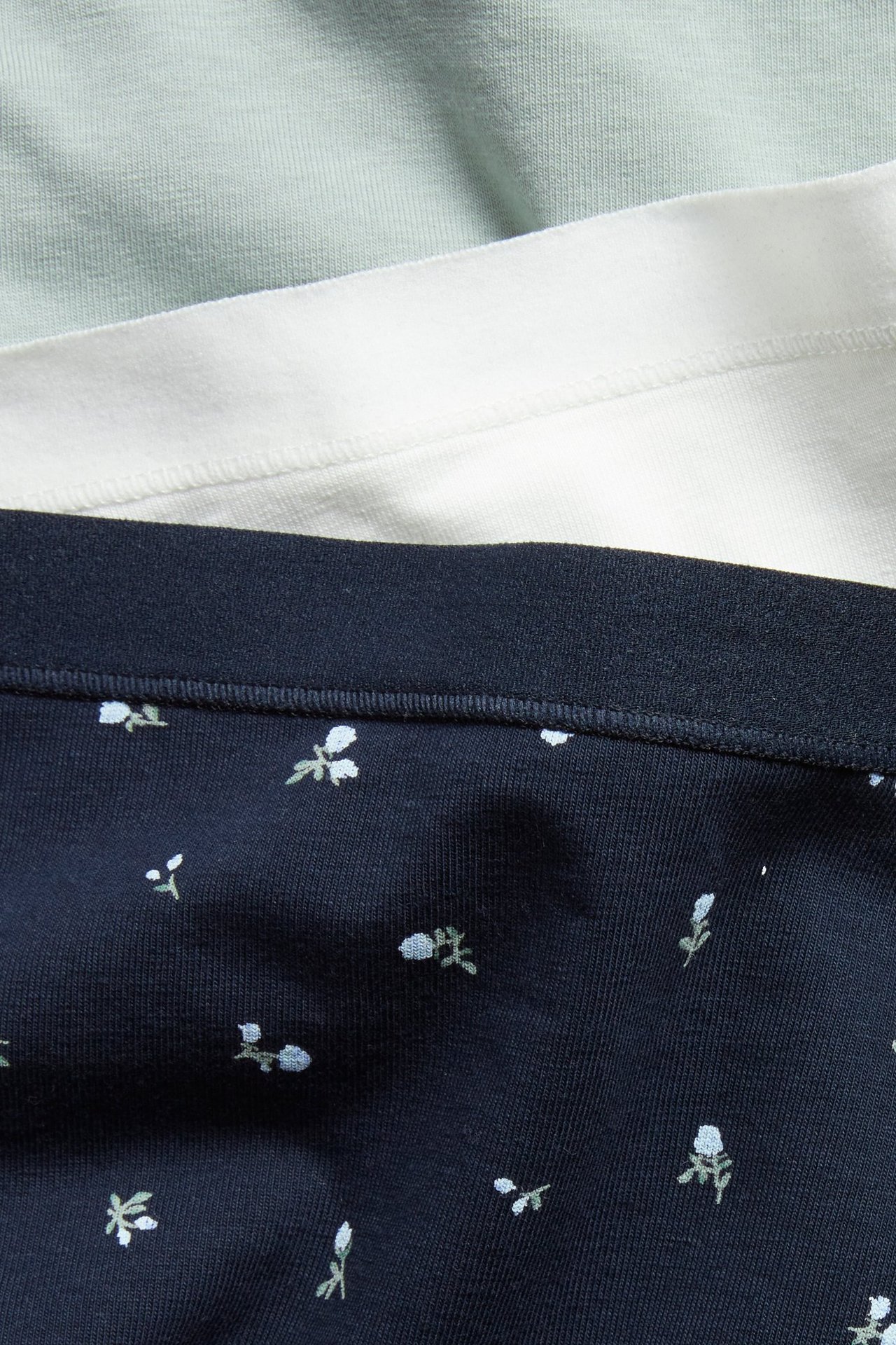 Forfra, tre boxertruser: mørkeblå med hvitt blomstermønster, lys beige og lysegrønn.