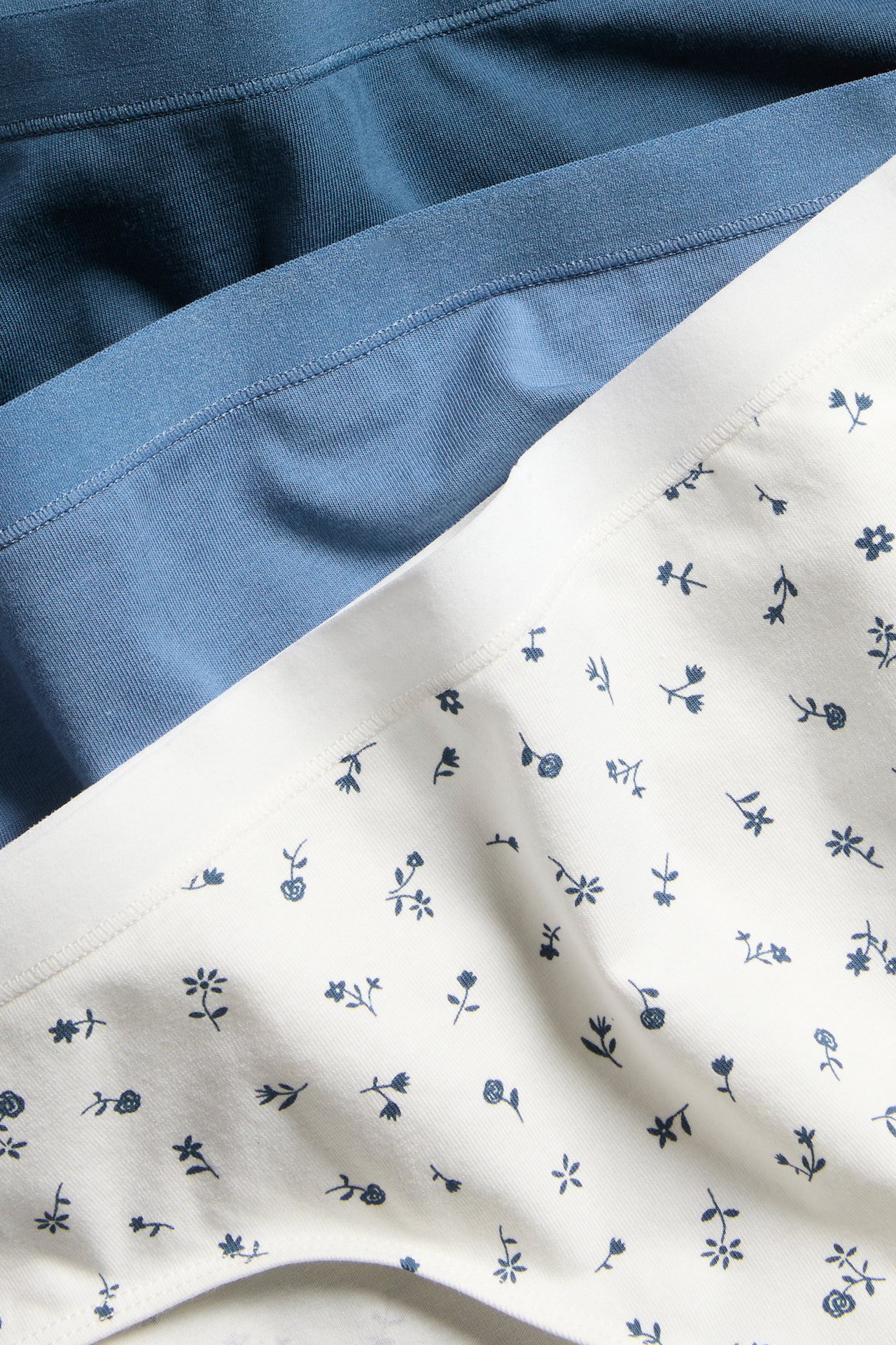 Nærbilde av kvinners 3-pakning truser: hvite med blått blomstermønster, pluss lyseblå og mørkeblå par.