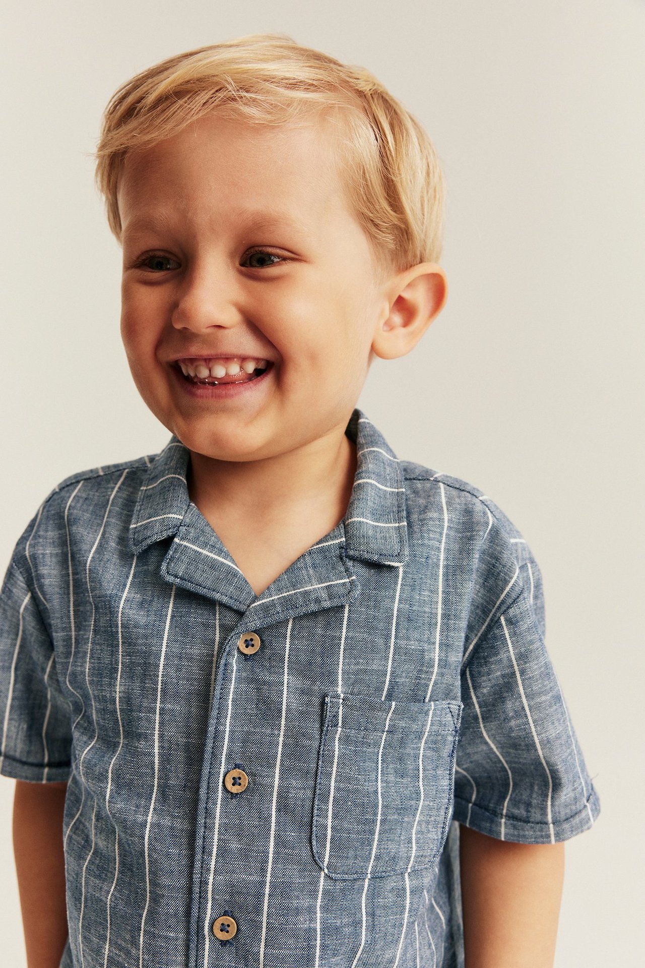 Widok z przodu uśmiechniętego dziecka w niebieskiej koszuli w paski z kołnierzykiem i kieszenią.