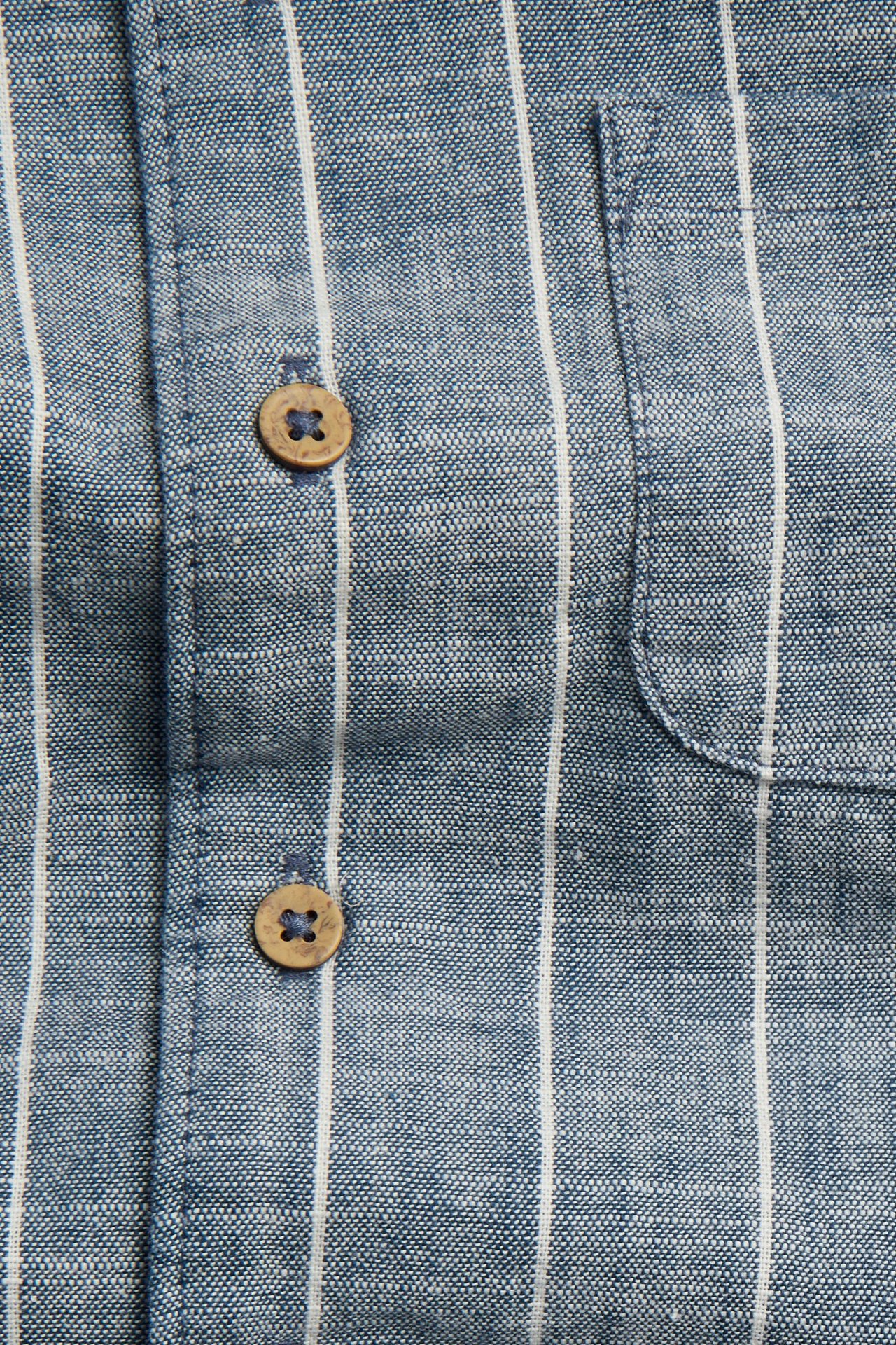 Zbliżenie na niebieską bawełnianą koszulę w białe paski, z kieszonką i drewnianymi guzikami.