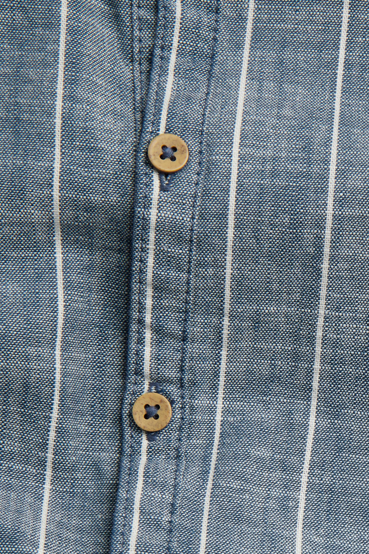 Närbild av en blå och vitrandig vävd bomullsromper med två bruna träknappar.