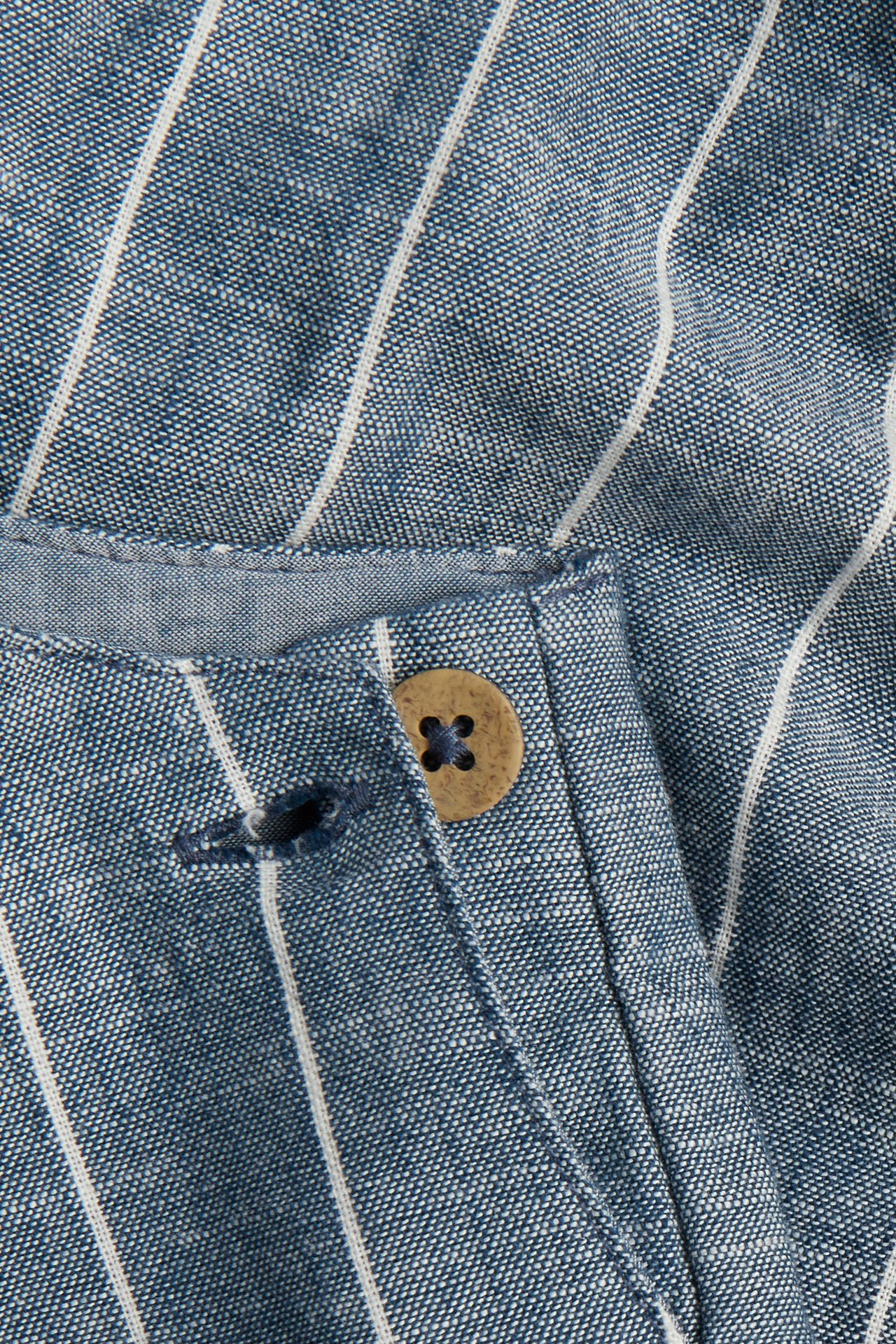 Nærbilde av blå- og hvitstripede vevde bomullsselebukser med brun knappelukking.