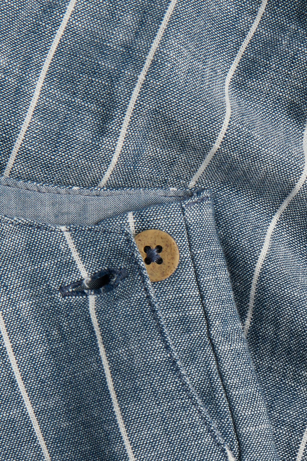 Nærbilde av blå- og hvitstripede vevde bomullsselebukser med brun knappelukking.