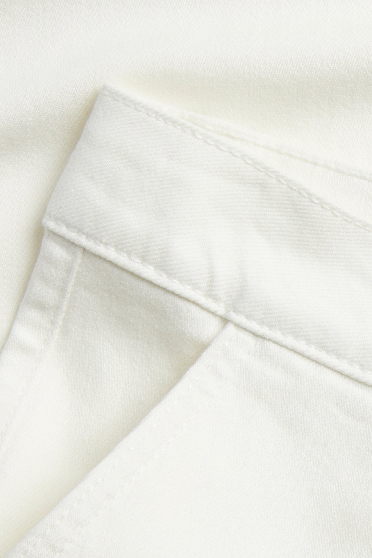 Lähikuva luonnonvalkoisista twill-housuista, jotka esittävät vyötärönauhan ja taskun aukon.
