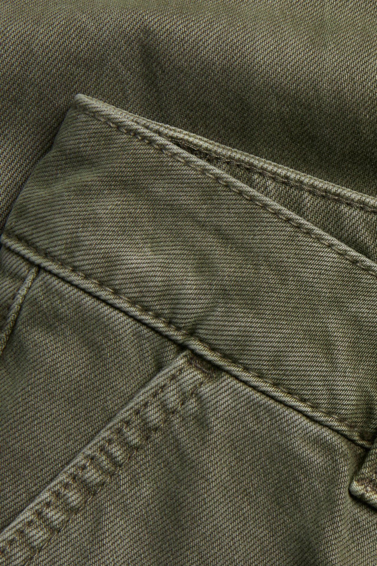 Lähikuva vihreistä puuvillatwill-housuista, näyttää kankaan, saumat ja taskun yksityiskohdan.