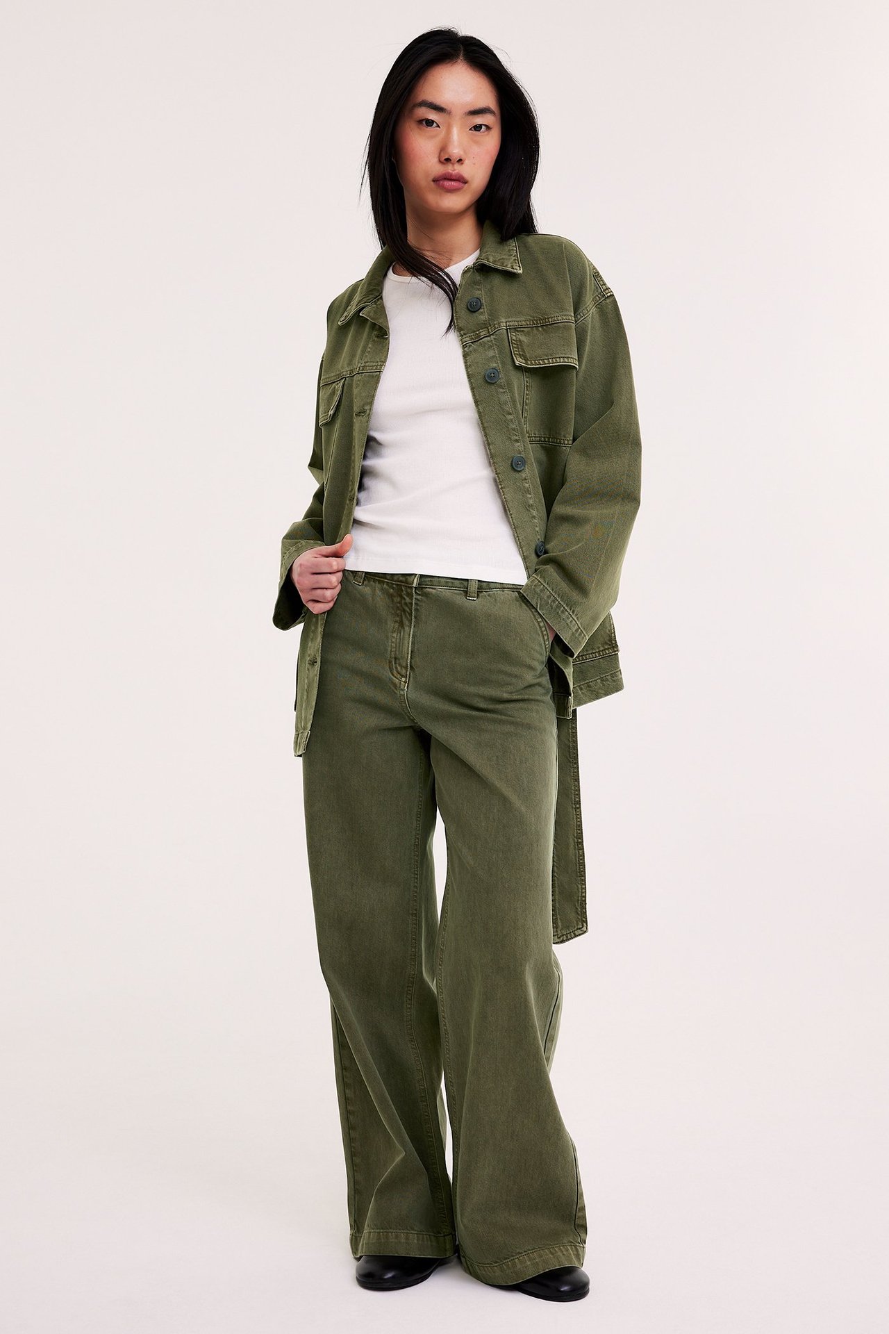 Nainen edestäpäin vihreissä leveälahkeisissa twill-housuissa, yhteensopivan takin ja valkoisen t-paidan kanssa.