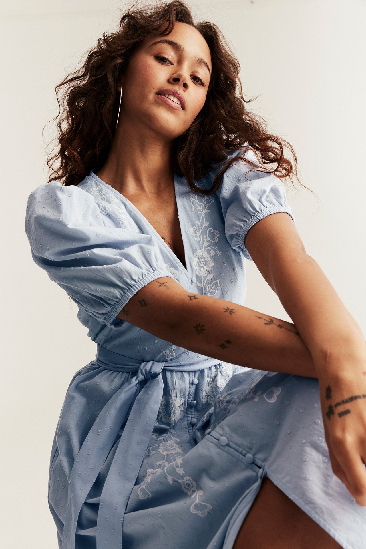 Widok z przodu: kobieta w jasnoniebieskiej bawełnianej sukience z haftem, bufiastymi rękawami i wiązaną talią.