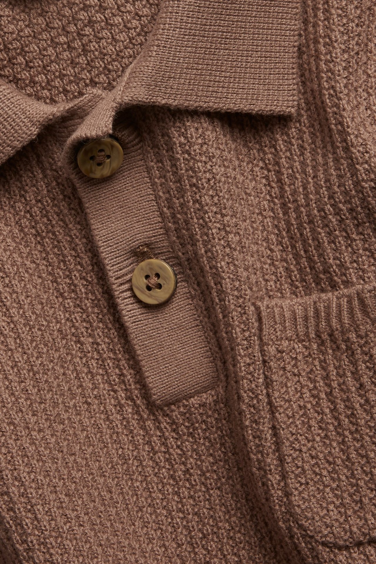 Lähikuva edestä ruskeasta neulotusta lyhythihaisesta pikeepaidasta, jossa kaulus, nappilista ja rintatasku.