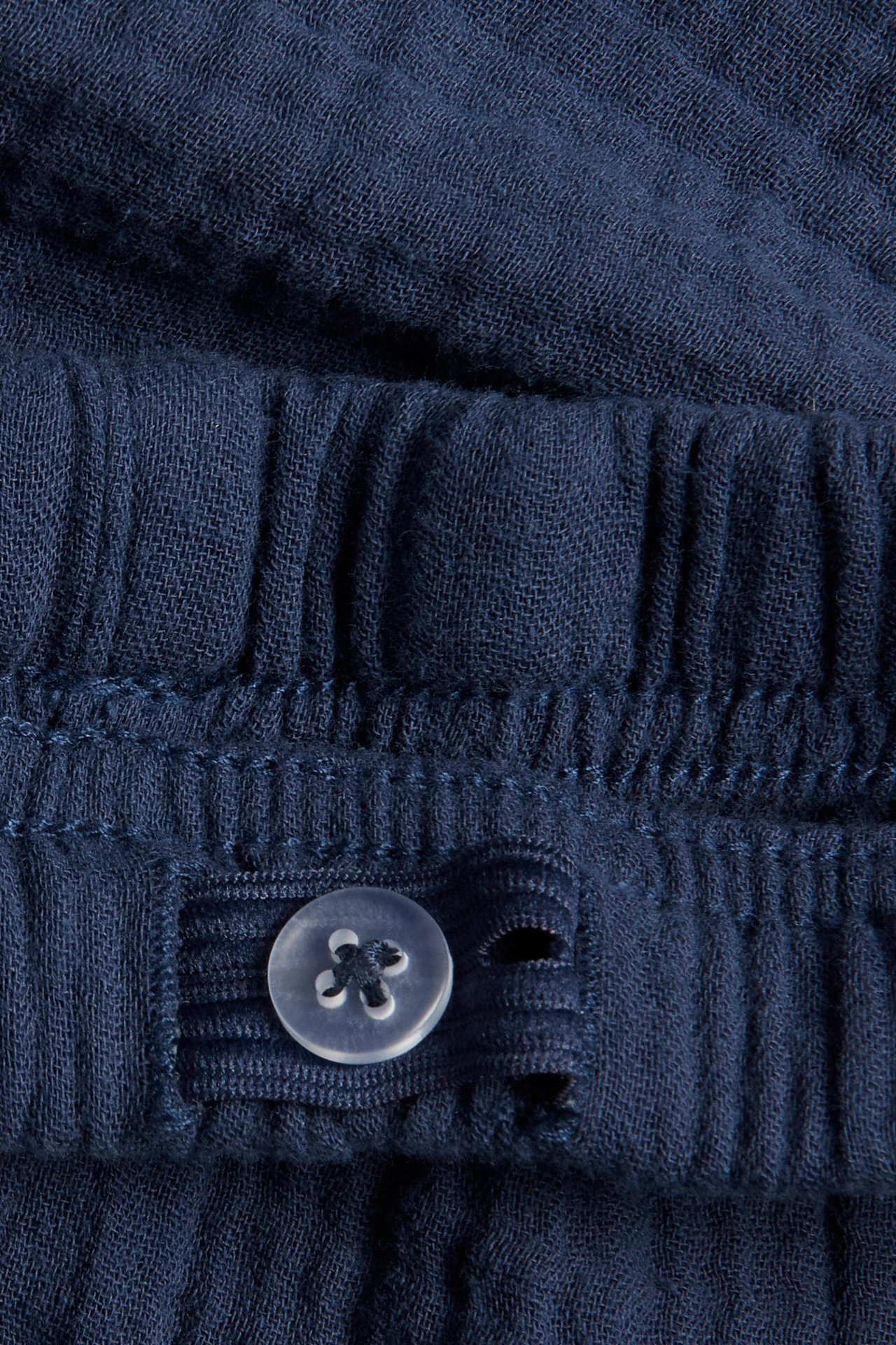 Lähikuva sinisistä musliinishortseista, joissa näkyy säädettävä joustovyötärö ja läpinäkyvä nappi.