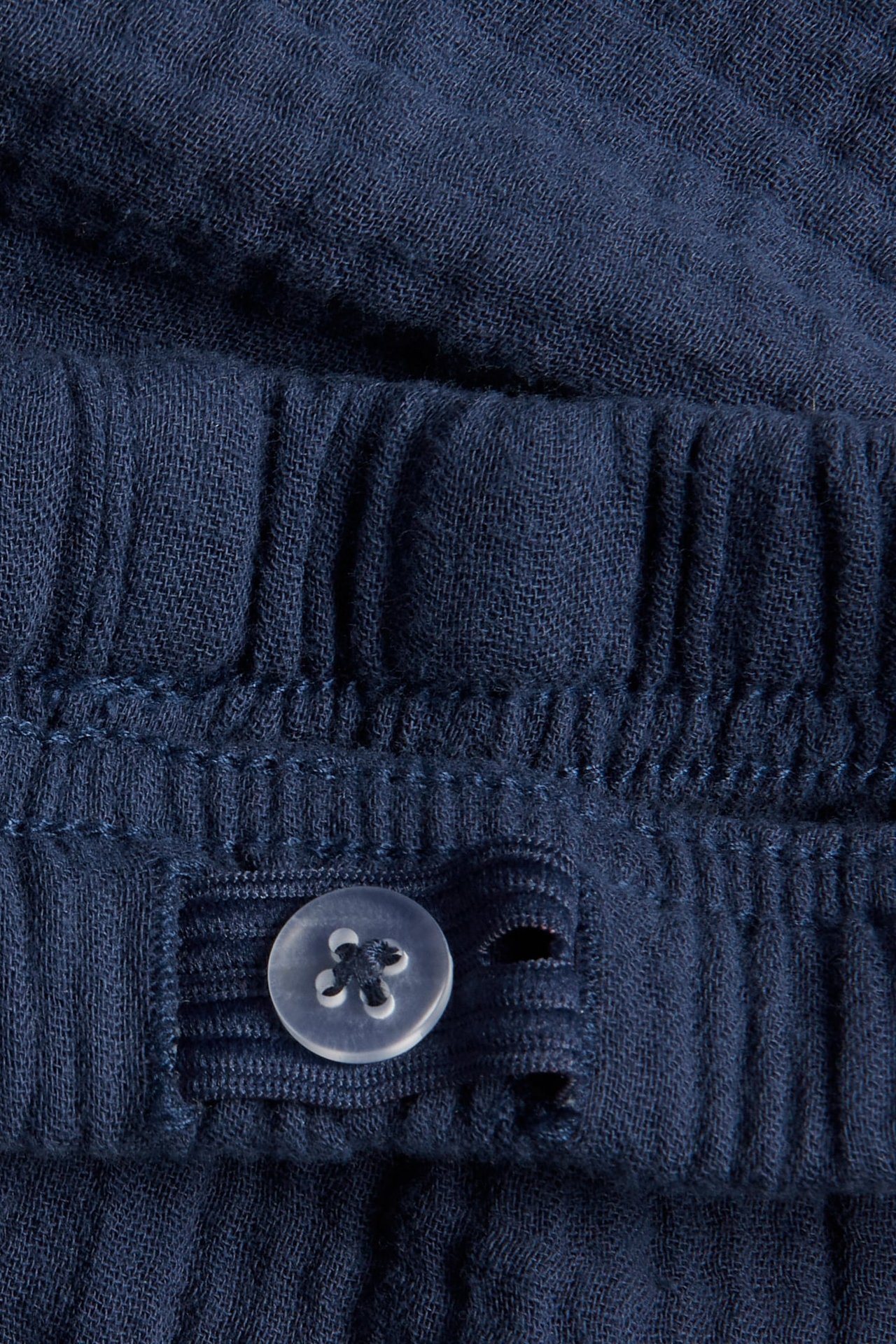 Närbild av blåa muslinsorts som visar en justerbar resår i midjan med en transparent knapp.