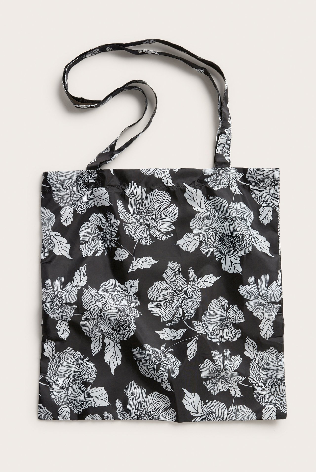 Edestäpäin näkymä mustasta polyester ostoskassista, jossa valkoinen kukkakuvio ja kaksi olkahihnaa.