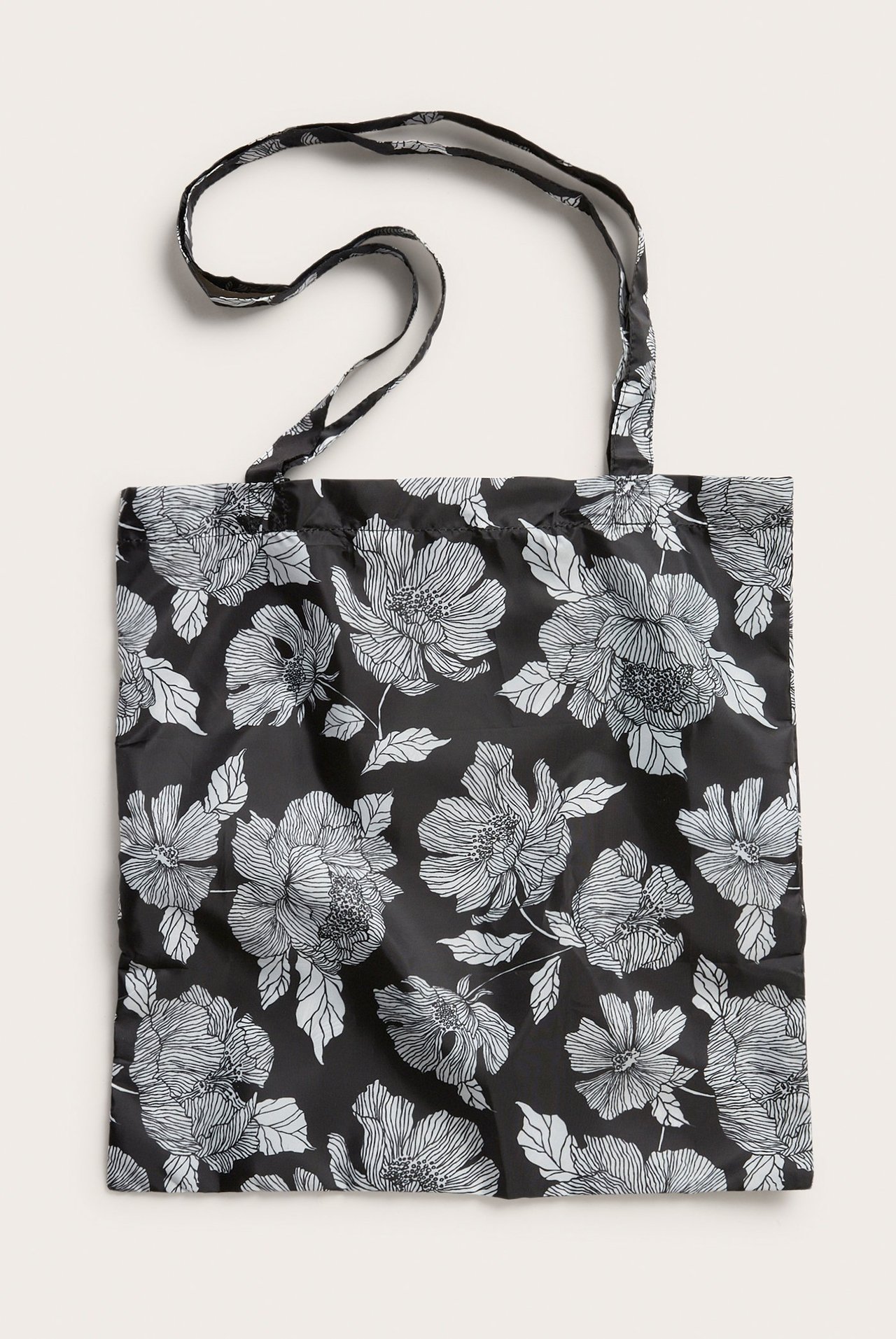 Framifrån syns en svart shoppingväska i polyester med vitt blommönster och två axelband.