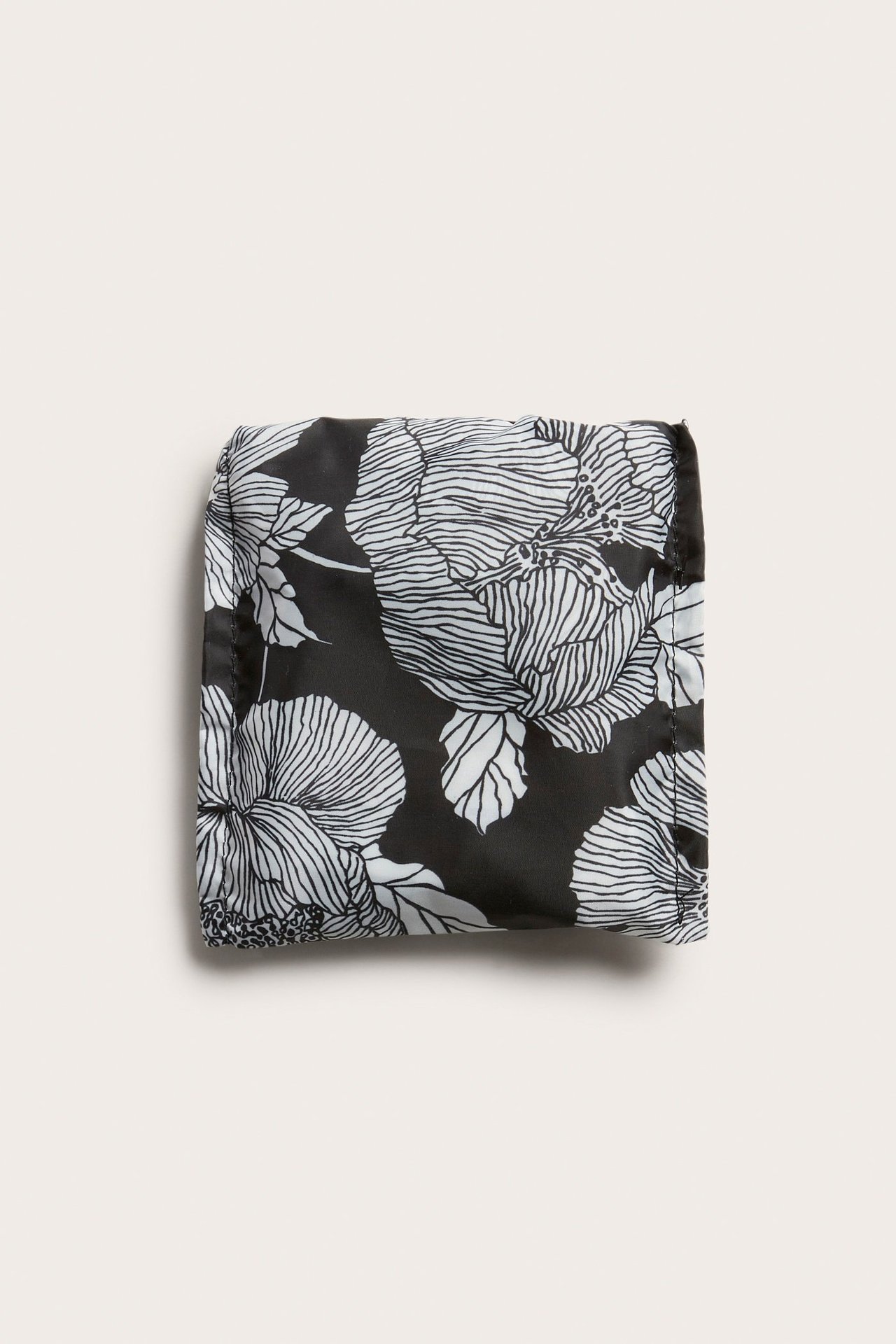 Uppifrån vy av en hopvikt svart shoppingväska i polyester med vitt blommönster.
