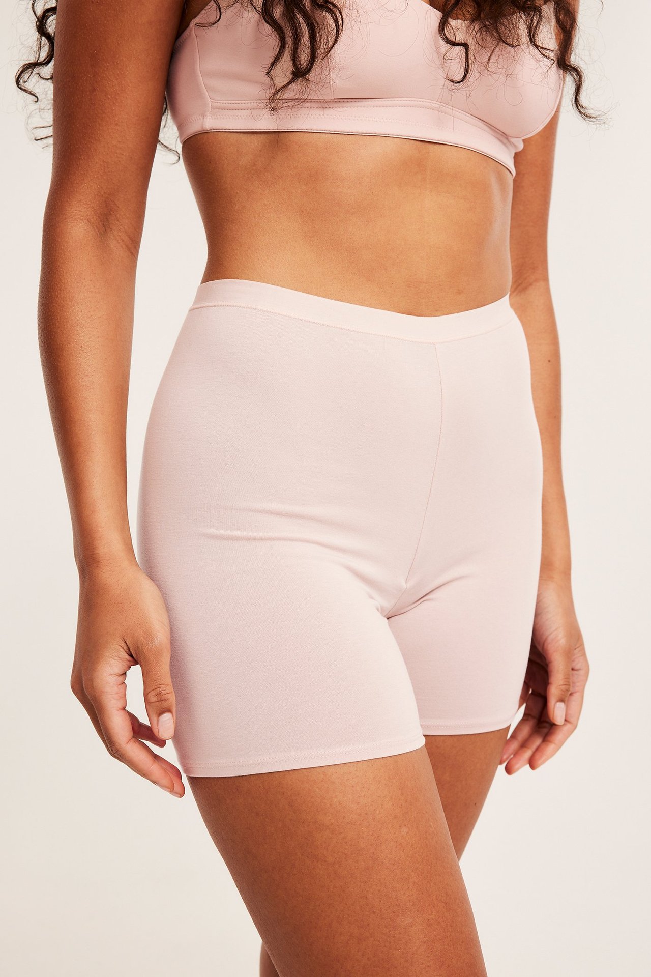 Sidebilde av en kvinne iført lyserosa høylivede bomullsshorts og en lyserosa BH.