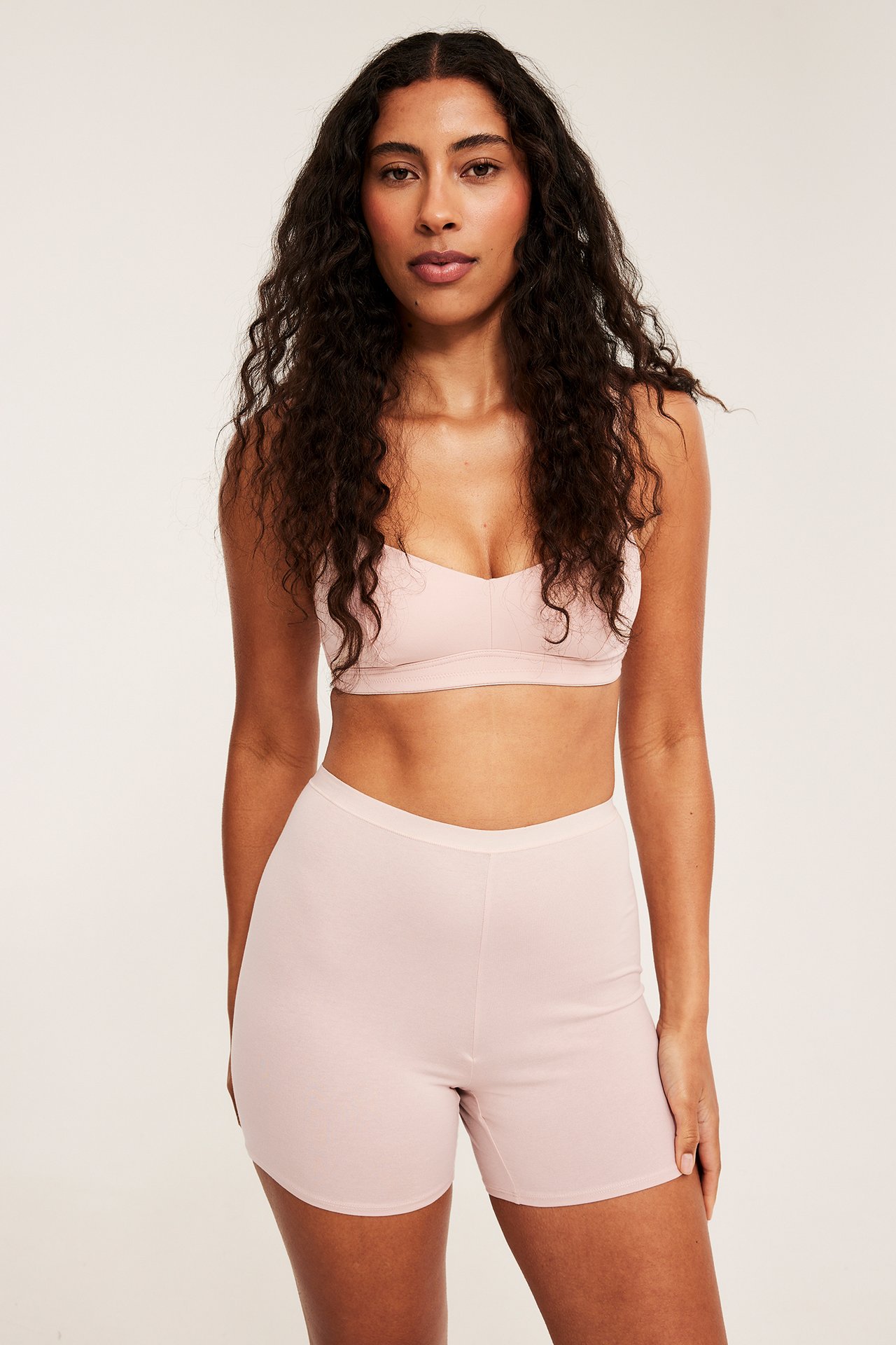 Frontbilde av kvinne i lys rosa høywaistede bomullsshorts og matchende bralette.