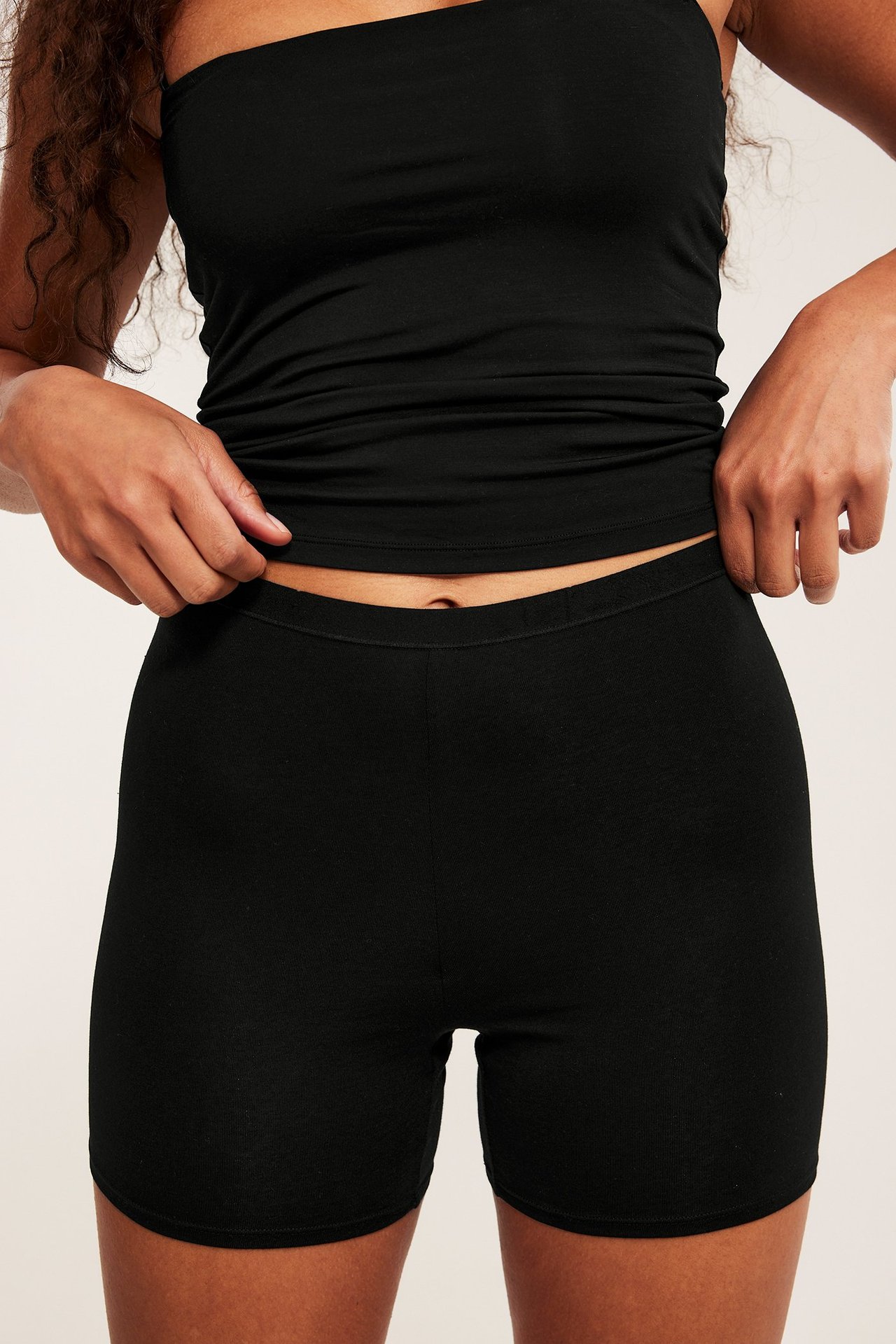 Frontutsikt: kvinne i svarte shorts-truser av bomull med høyt liv og en svart stroppeløs bandeau-topp.