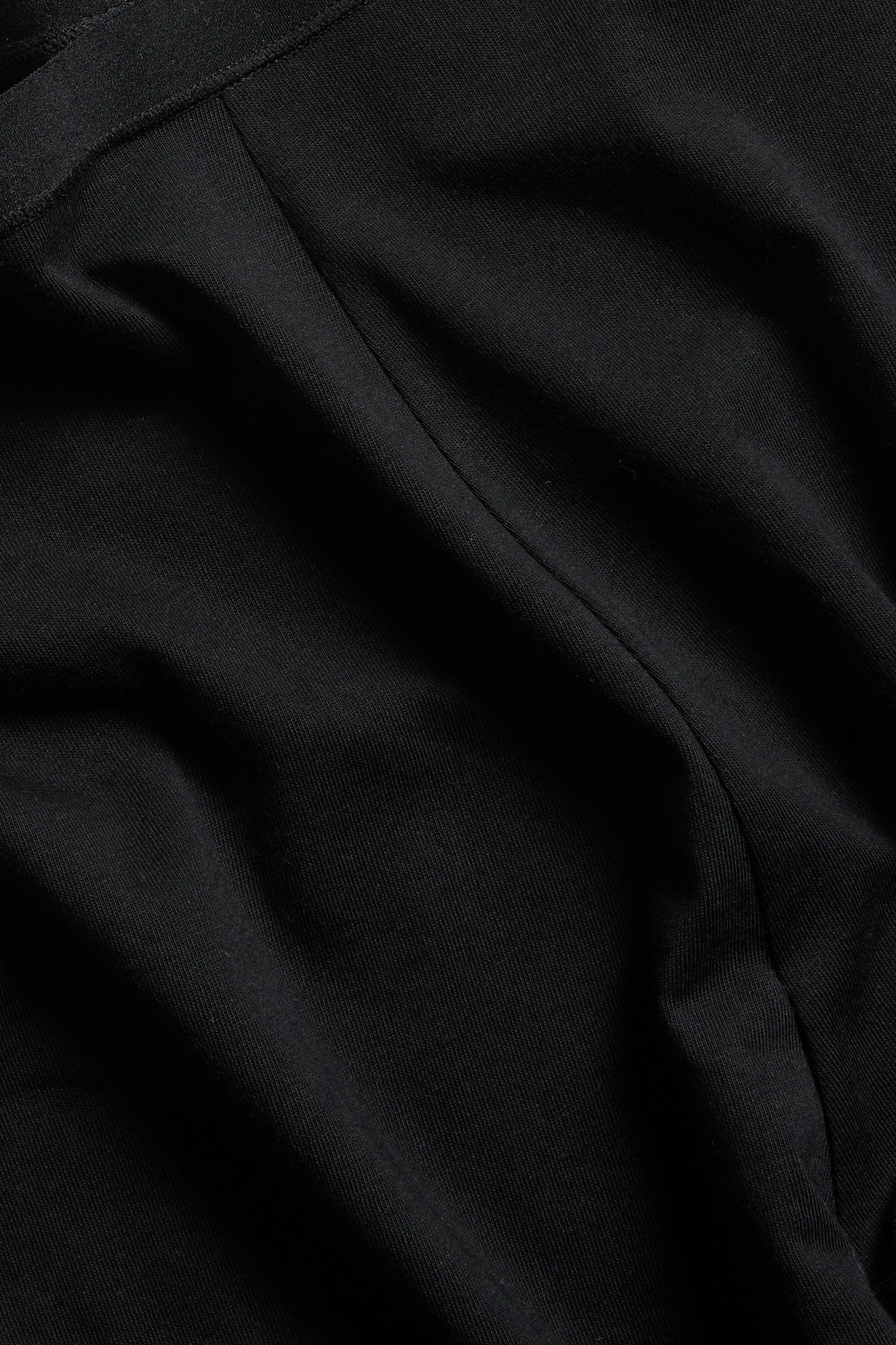 Nærbilde av svarte bomullsshorts med elastisk linning og synlig søm.