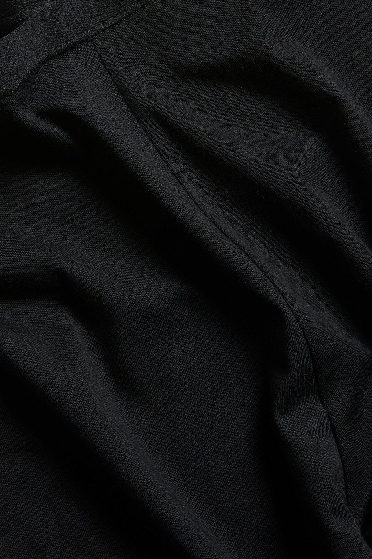 Nærbilde av svarte bomullsshorts med elastisk linning og synlig søm.