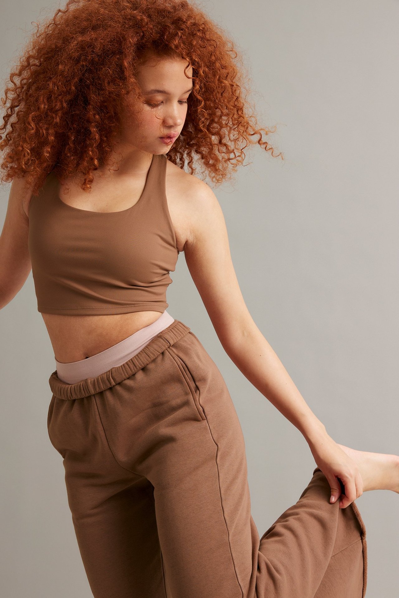 Etusivukuva naisesta ruskeassa lyhyessä urheilutopissa ja ruskeissa löysissä verryttelyhousuissa.