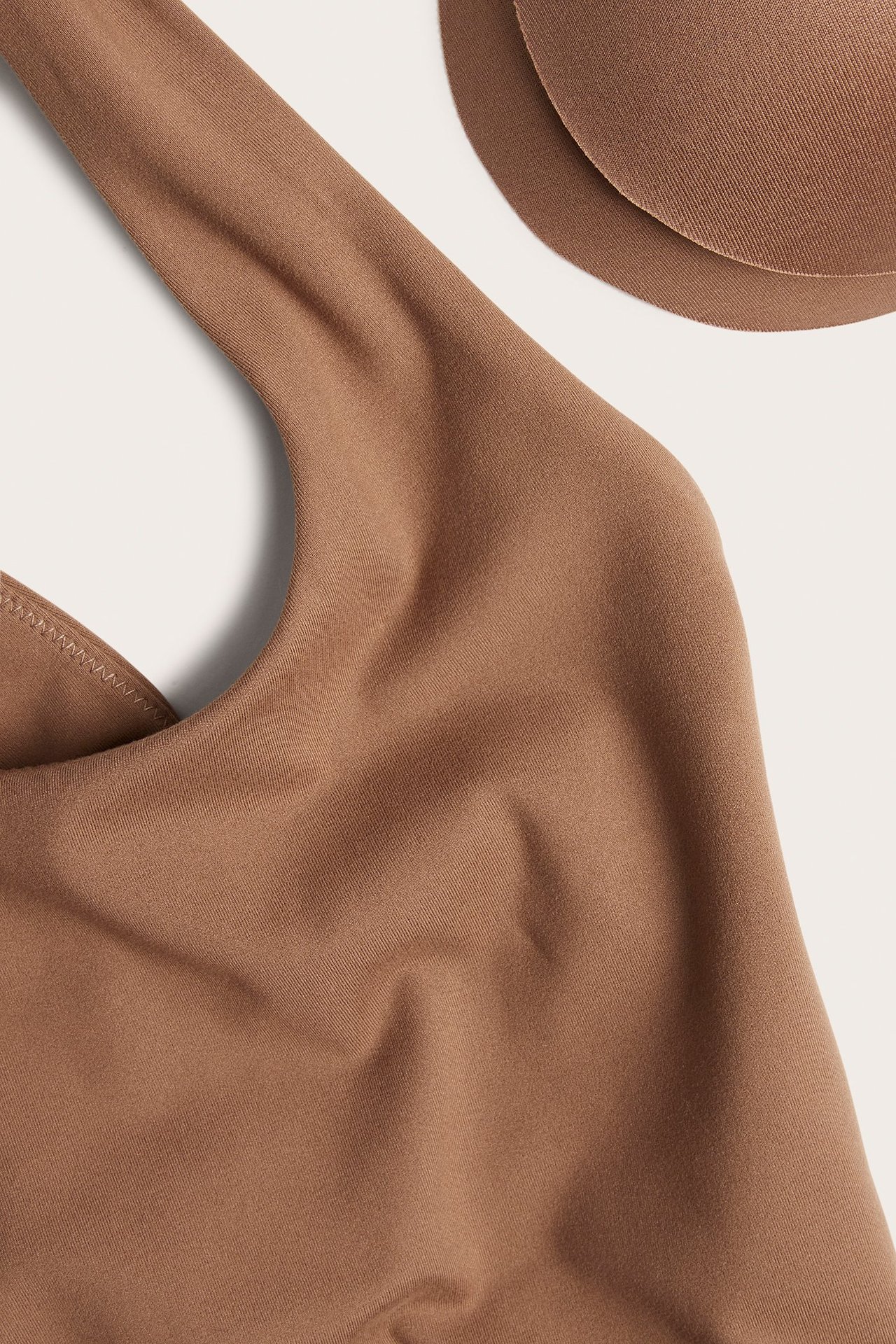 Zbliżenie brązowego, jednolitego topu sportowego z ramiączkiem i dwiema okrągłymi, wyjmowanymi wkładkami.