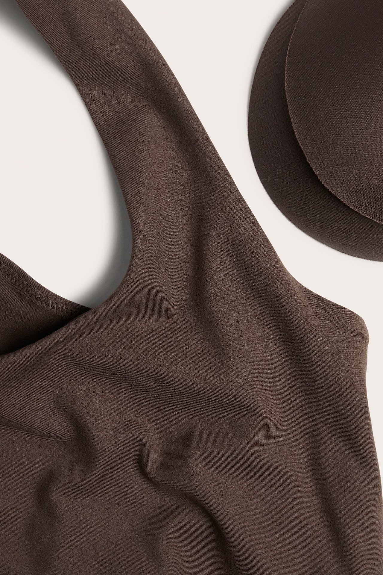 Zbliżenie na brązowy top sportowy z szerokimi ramiączkami i dwoma brązowymi, wyjmowanymi wkładkami.