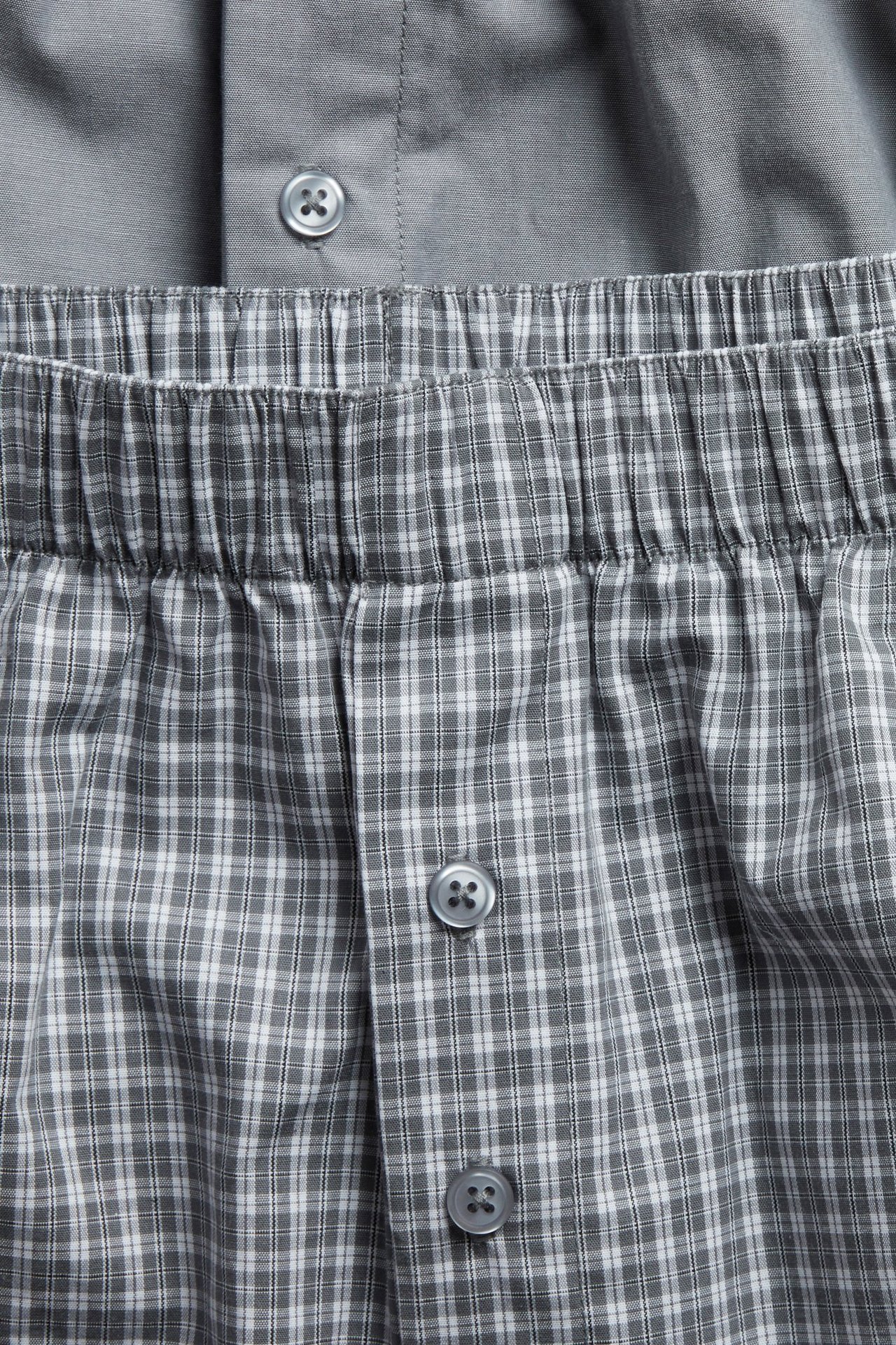 Närbild: herrars grårutiga boxershorts i vävt tyg, resår i midjan, knäppbar gylf. En enfärgad grå kalsong.
