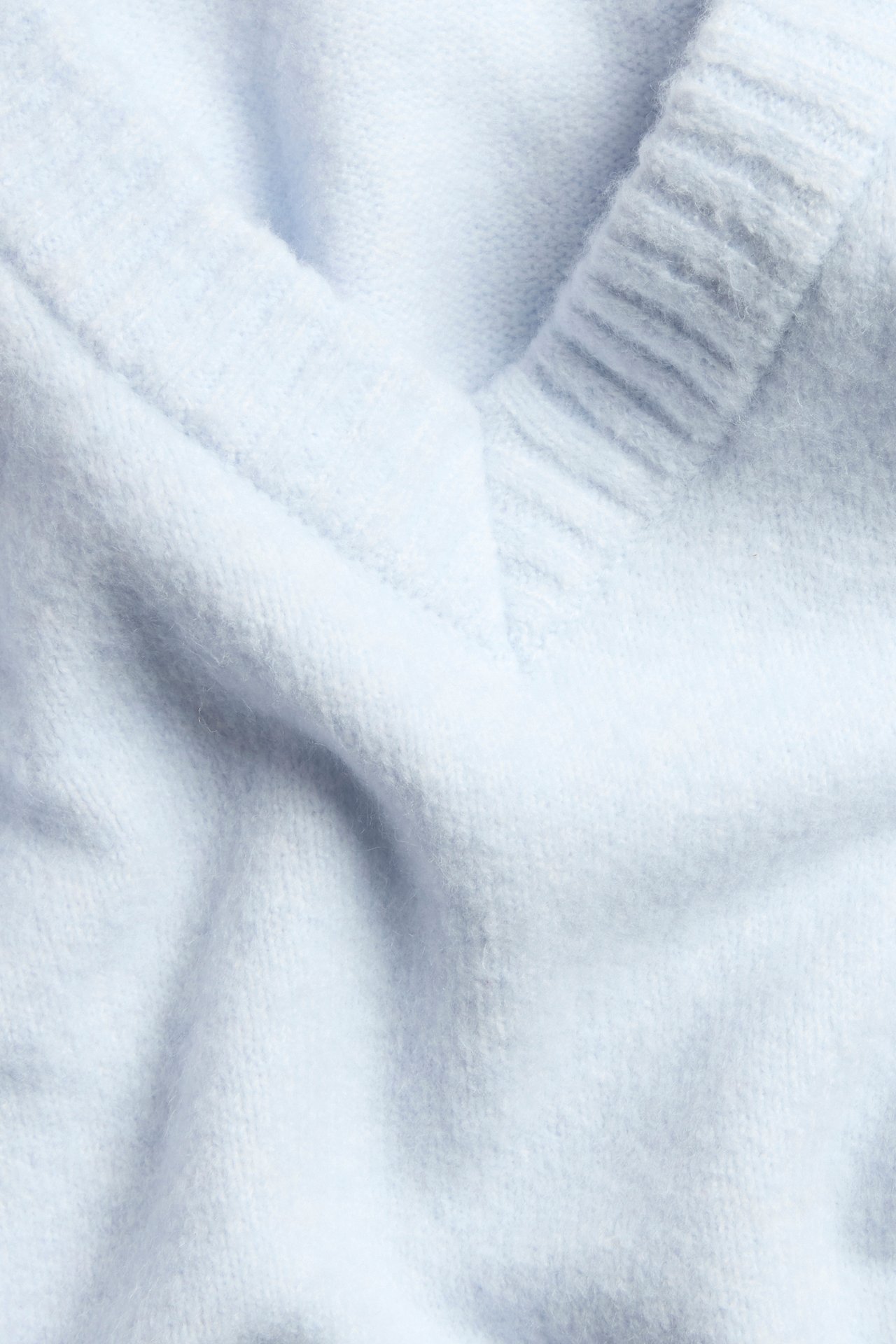 Nærbilde av en lyseblå strikket V-halsgenser, som viser ribbekanten og den myke teksturen.