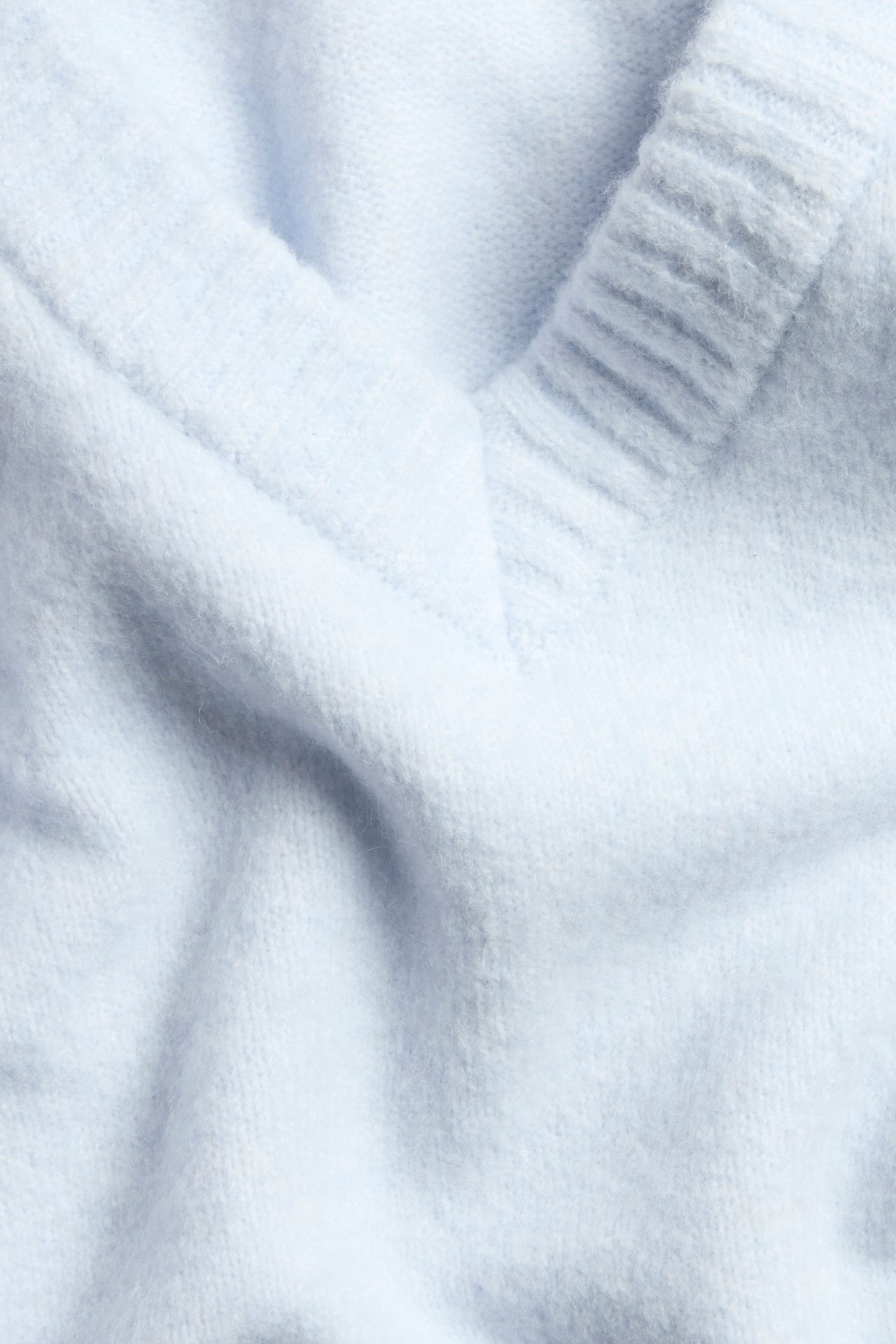 Zbliżenie na jasnoniebieski dzianinowy sweter z dekoltem w serek, pokazujące ściągacz i miękką fakturę.