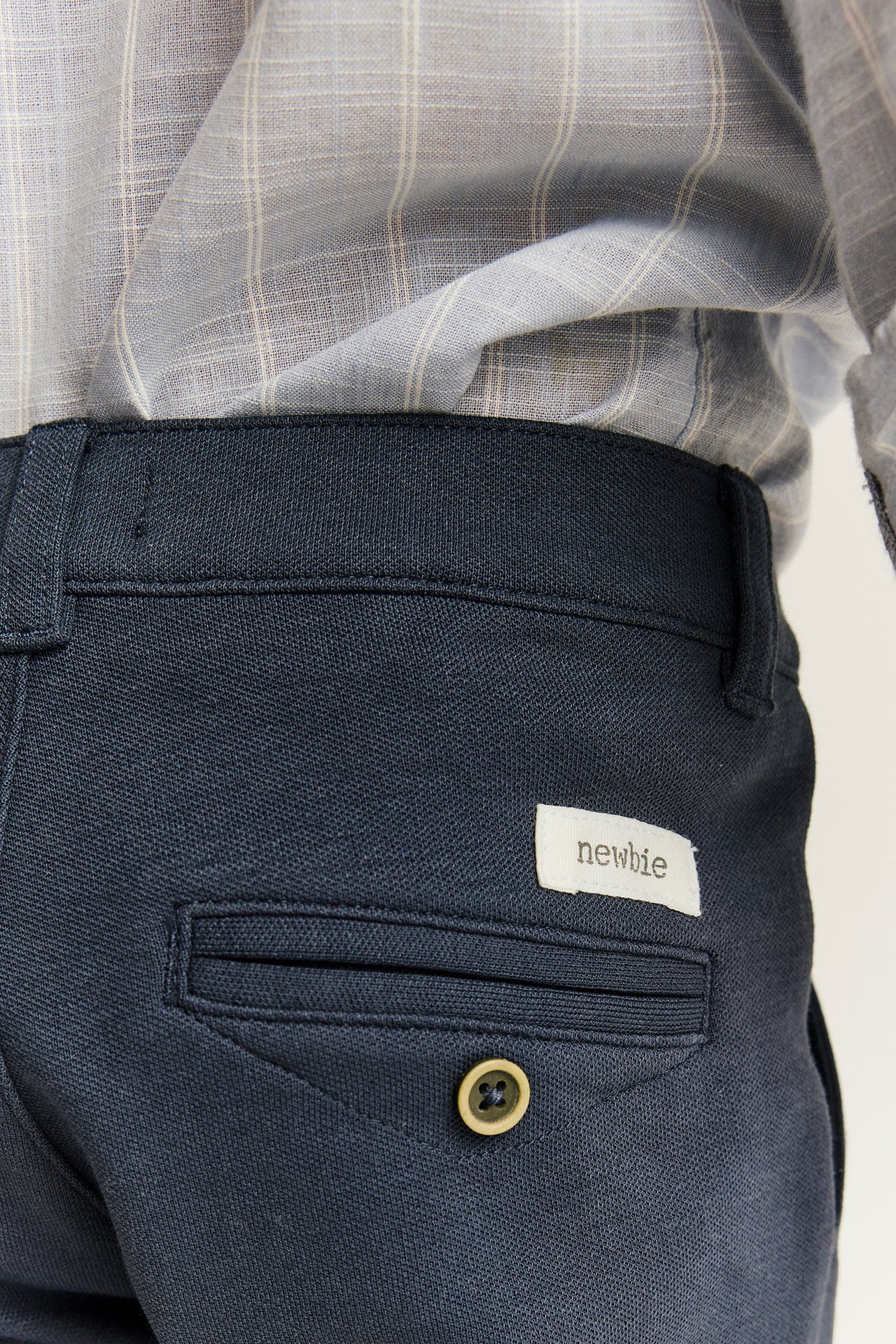 Nærbilde bakfra av et barn i mørkeblå bukser med dekorativ knapp og en grårutete skjorte.