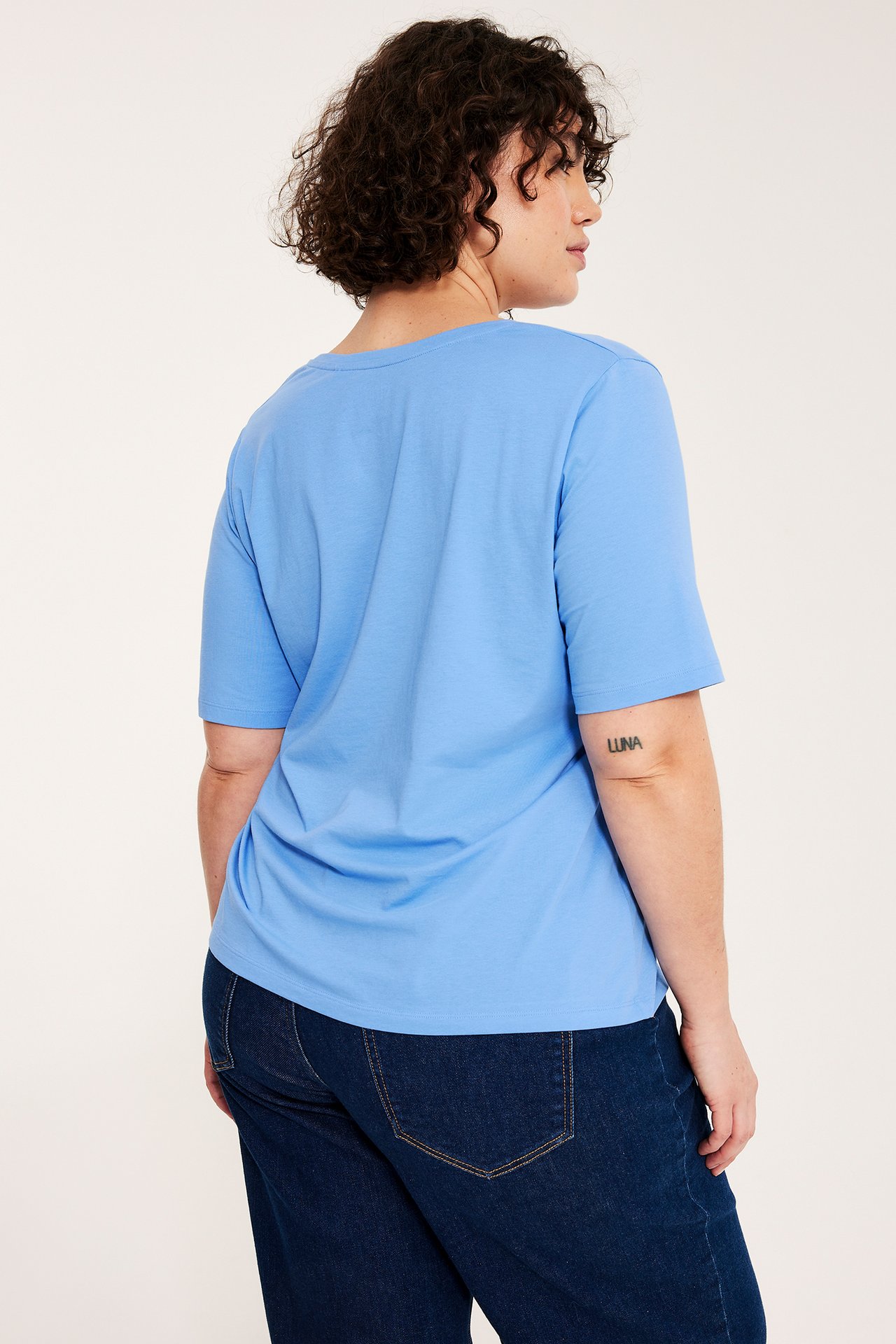 Naisen takaa: yllään vaaleansininen lyhythihainen T-paita ja tummansiniset farkut.