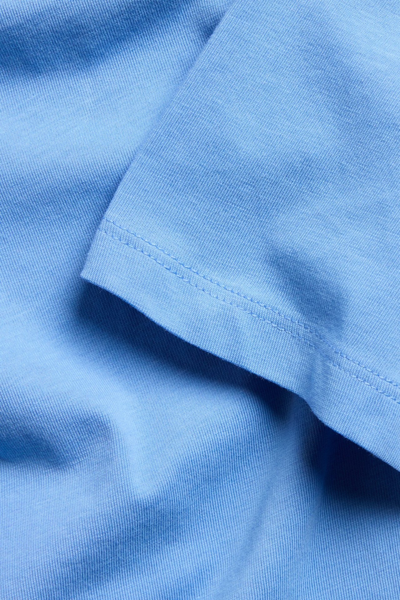 Zbliżenie na niebieską, jednolitą tkaninę T-shirtu, miękką mieszankę bawełny, z widocznymi szwami.