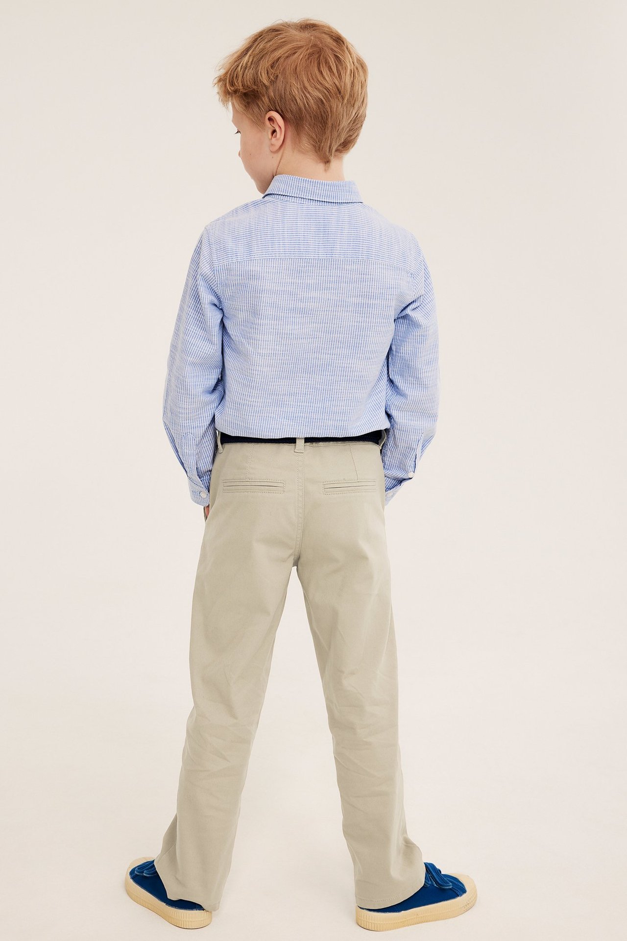 Ryggvy av ett barn i beiga bomullschinos, en blårandig skjorta och blå sneakers.