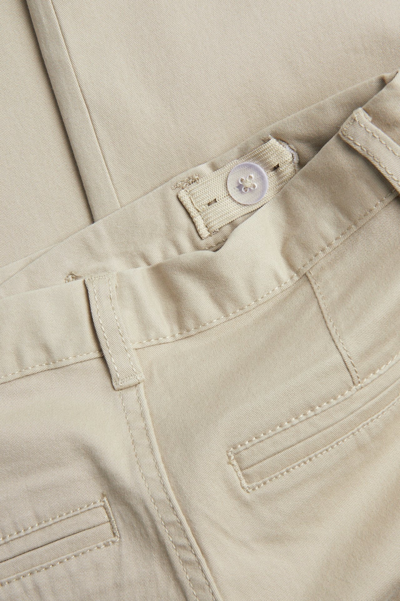 Lähikuva beigevärisistä puuvillatwill-lastenchinoista, näkyy säädettävä sisävyötärönappi ja takataskun yksityiskohdat.