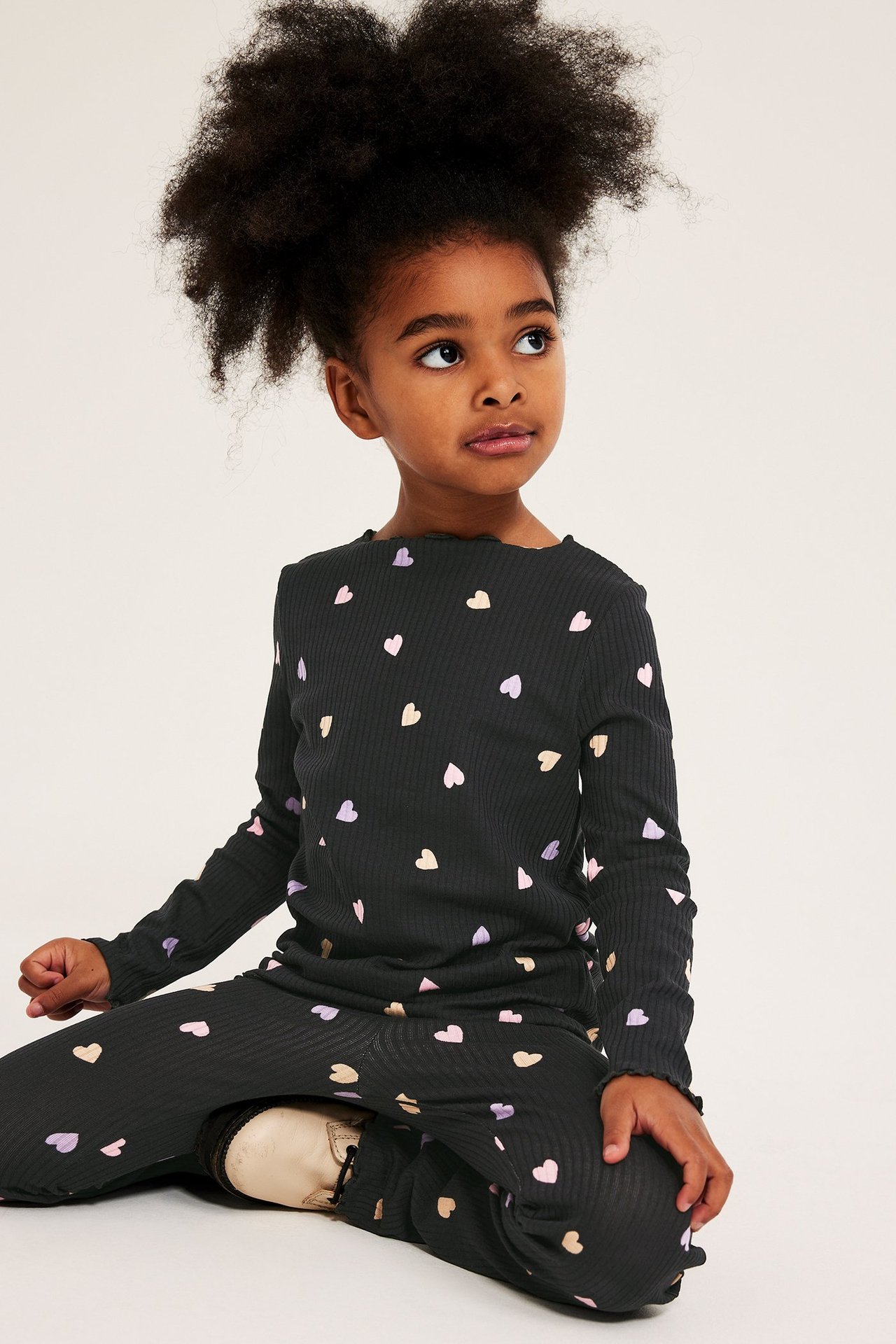 Frontvy: Kid bär en svart ribbad långärmad topp med hjärtmönster och matchande utsvängda byxor.
