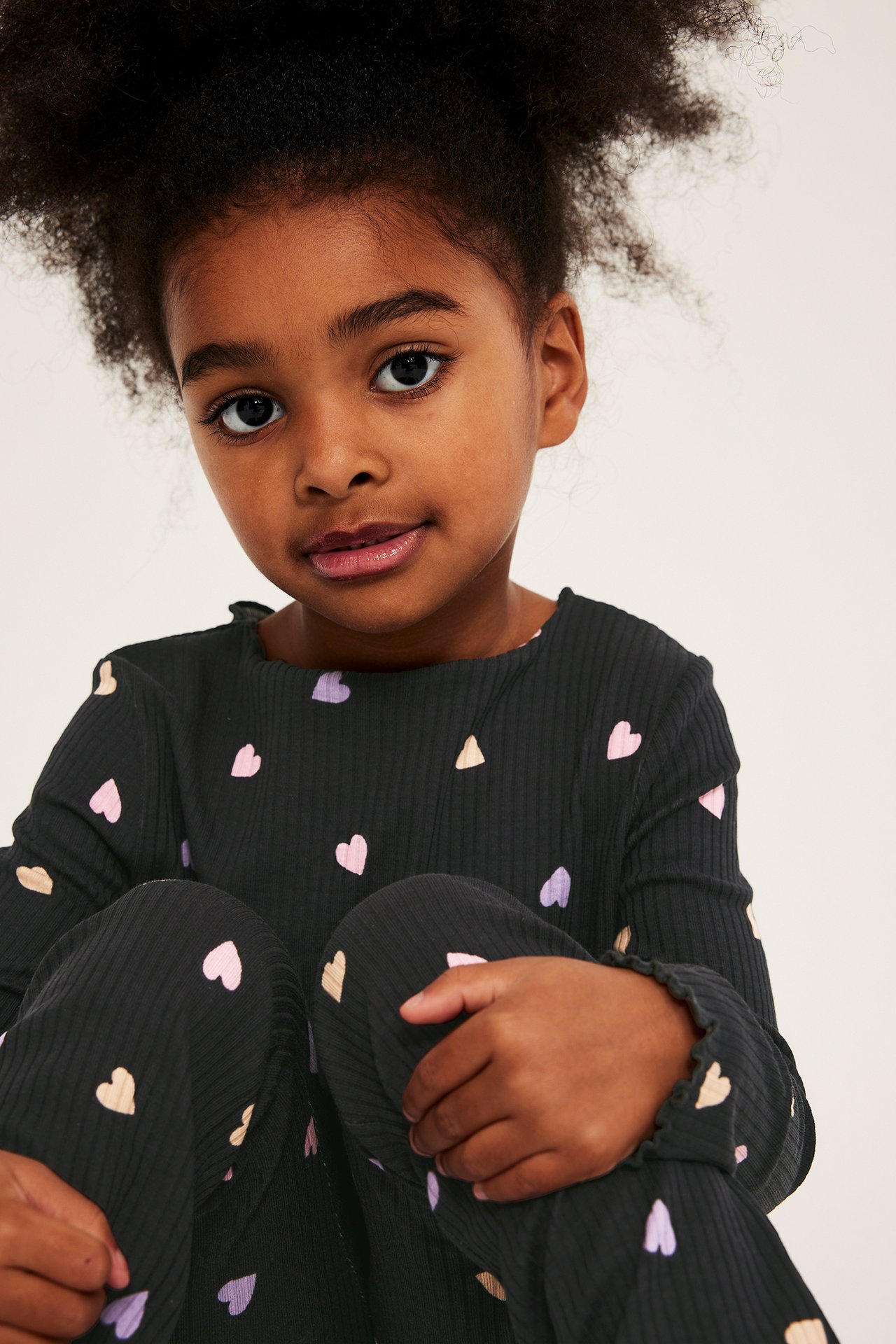 Frontutsikt, barn i svart ribbet langermet topp med rosa, lilla, beige hjerter og matchende bukse.