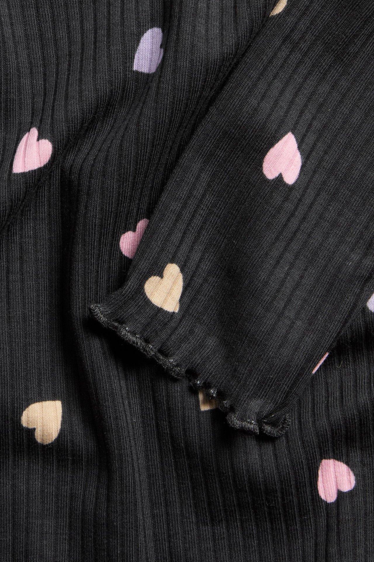 Zbliżenie czarnego prążkowanego topu z długim rękawem z różowymi, beżowymi i jasnofioletowymi sercami oraz mankietami typu babylock.