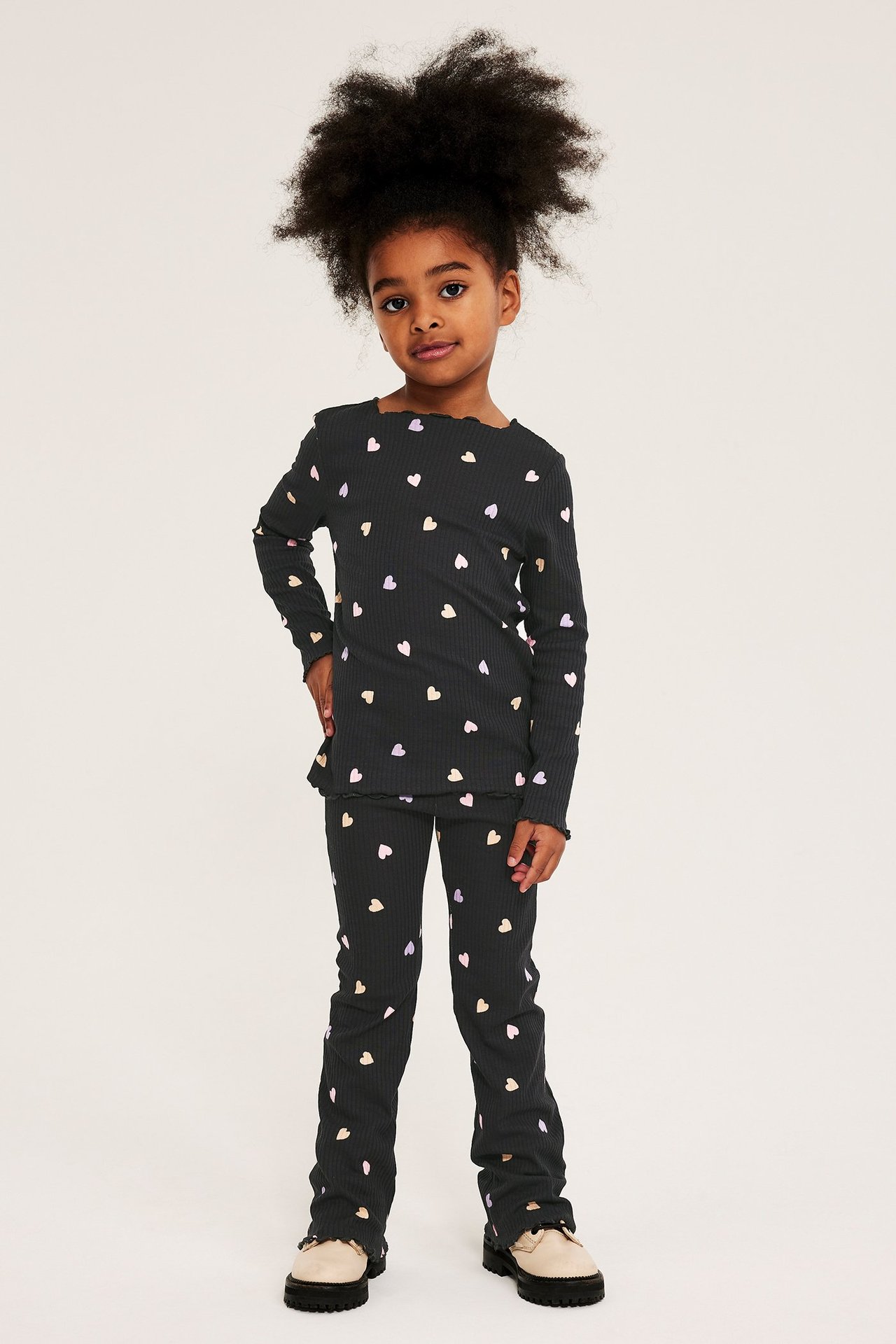 Forfra: et barn i svarte ribbestrikkede flare-leggings og matchende langermet topp med fargerike hjerteprint.