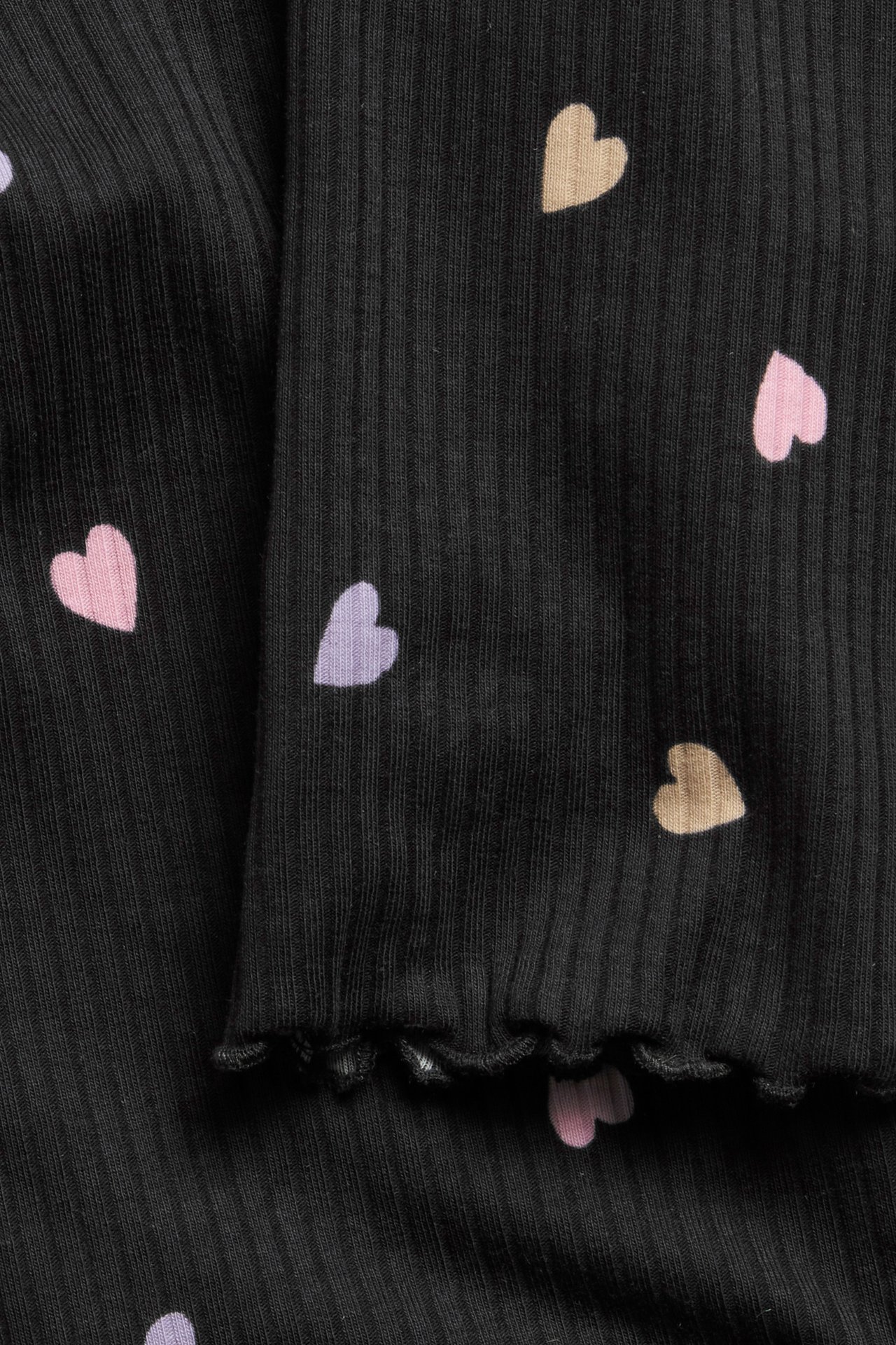 Nærbilde: Babyleggings i svart ribbet trikot med spredte rosa, lilla, beige hjerter og babylock-kant.