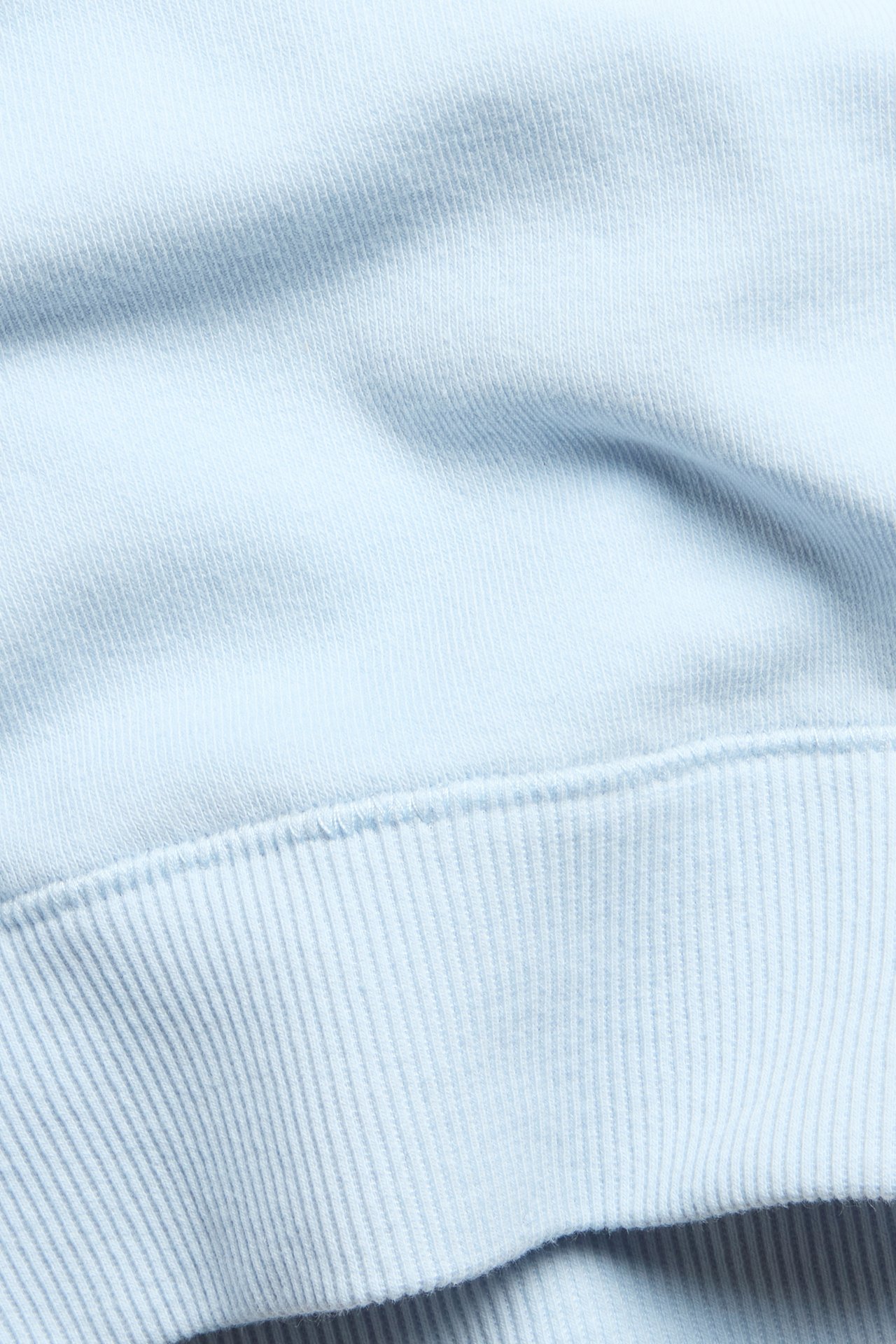 Nærbilde av lys blå ensfarget bomullsmix BH-topp stoff med ribbekant.