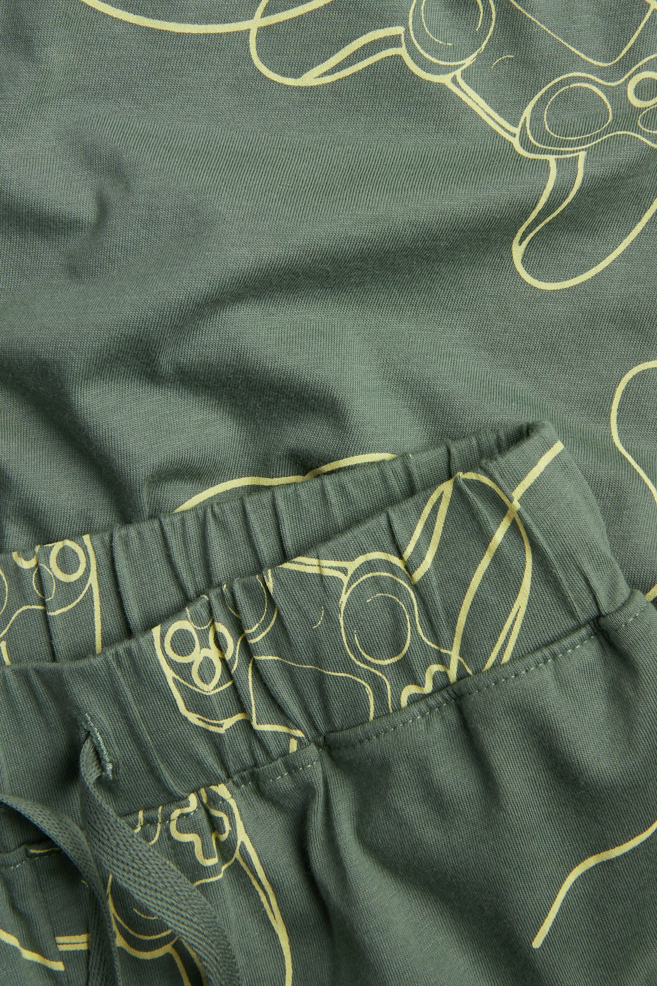 Närbild av gröna bomullspyjamas shorts med gult spelkontrolls mönster, elastisk midja och dragsko.