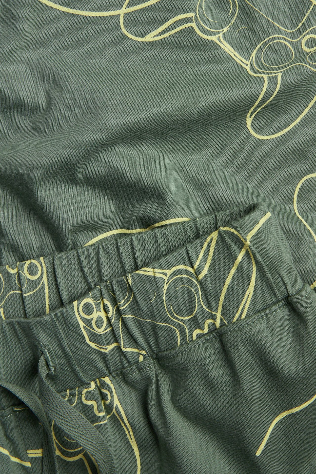 Zbliżenie na zielone bawełniane spodenki piżamowe z żółtym wzorem kontrolera gier, gumką, sznurkiem.