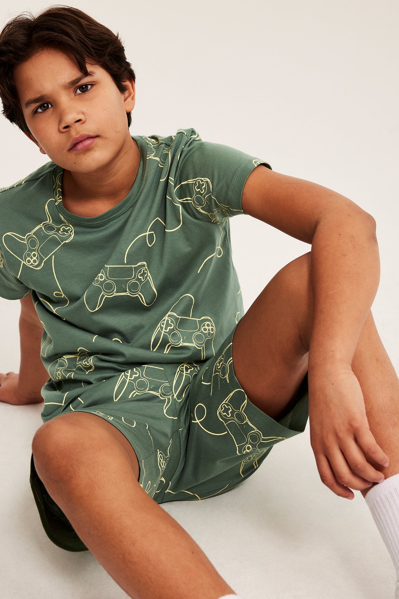 Chłopiec w zielonym piżamie z motywem gier, siedzi na podłodze, zbliżenie, widok z przodu.