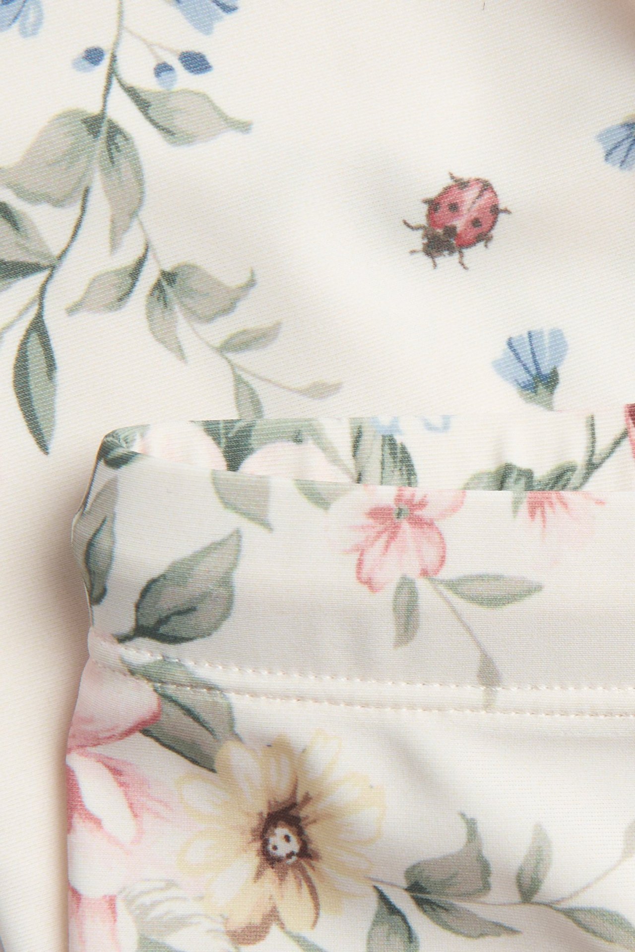 Zbliżenie na kremowe, kwieciste kąpielówki UV trzy czwarte z nadrukiem biedronki.